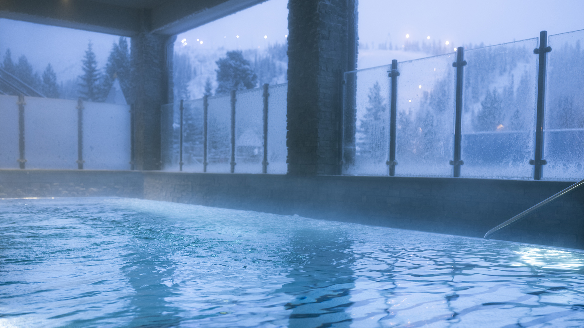 Uppvärmd utomhuspool med utsikt över snöiga berg och belysta skidbackar