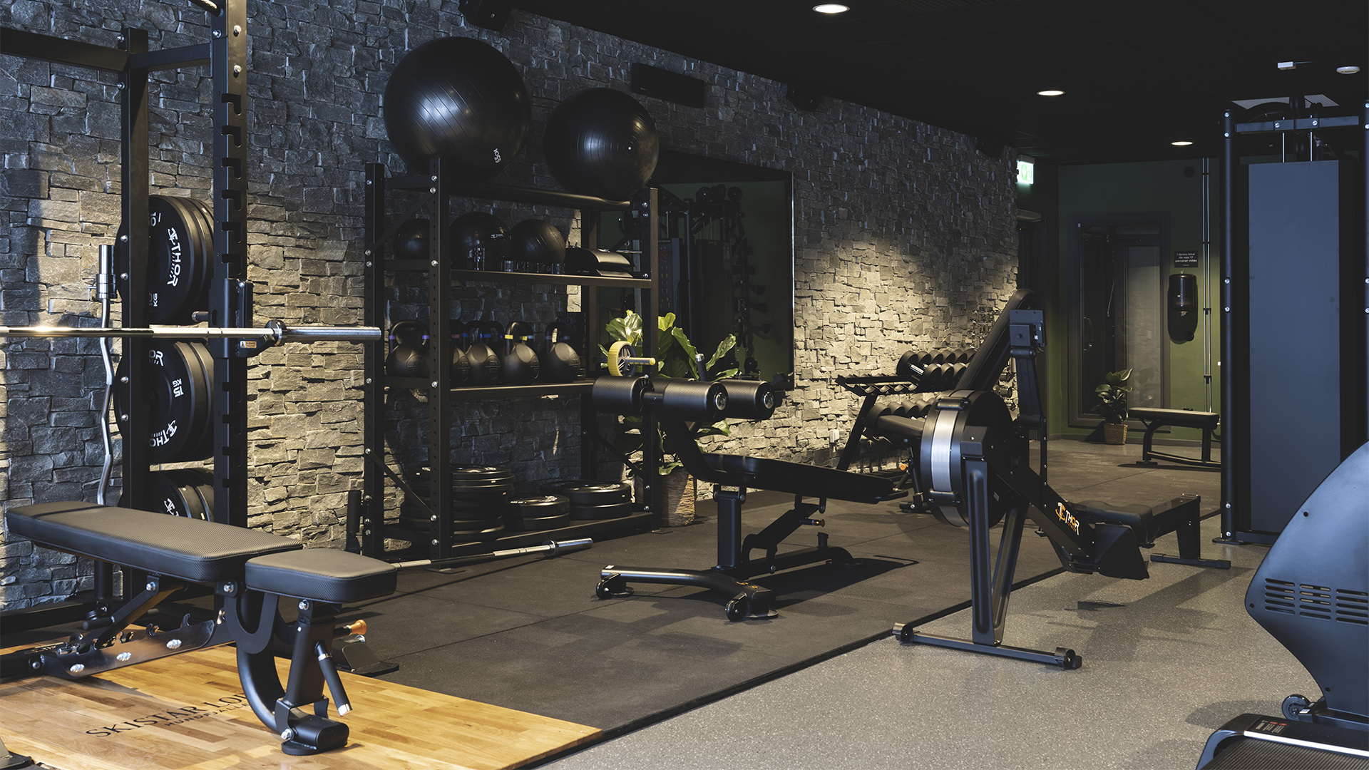 Modernt gym med styrketräningsutrustning och fria vikter i en stilren lokal med stenväggar