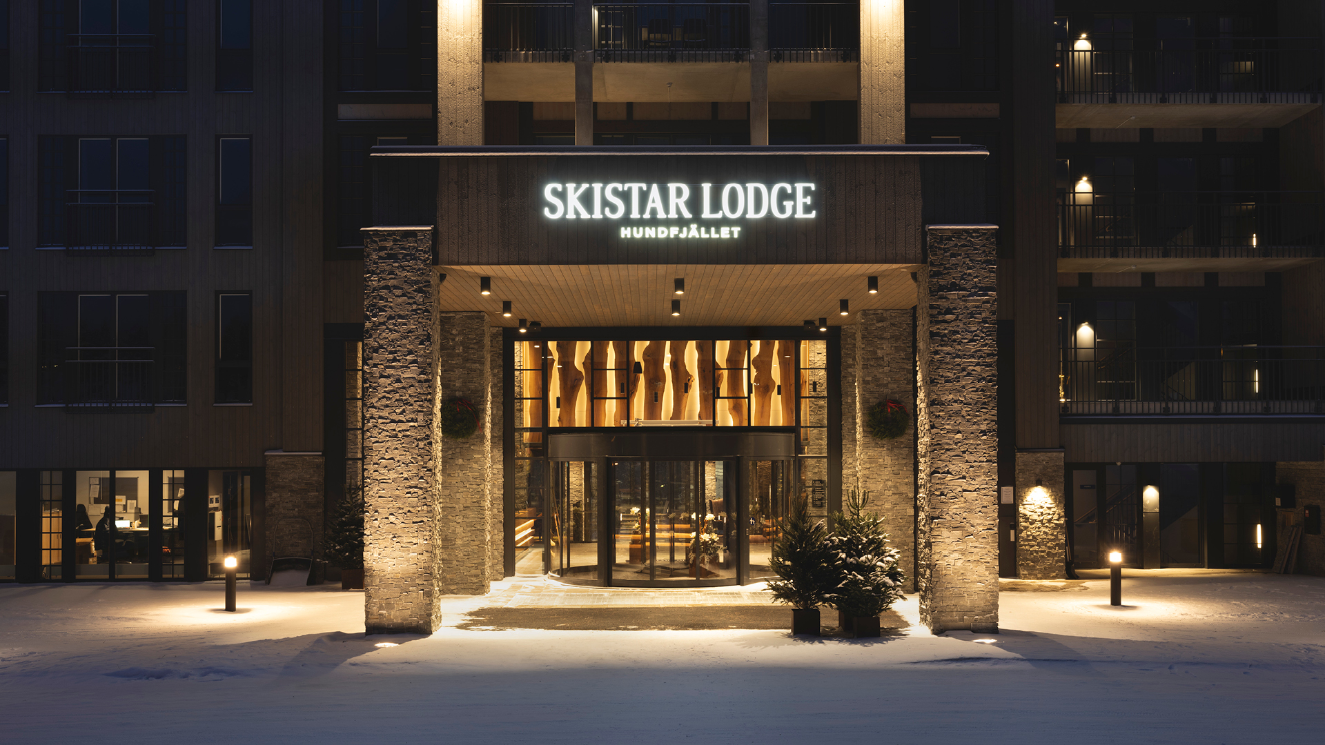 Entré till SkiStar Lodge Hundfjället på vintern, med snö på marken och belysning som framhäver byggnadens fasad