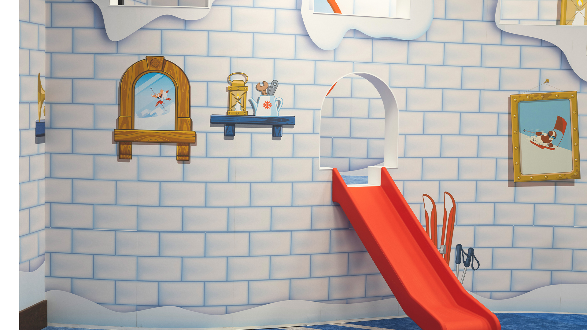 Lekfullt rum med snöslottstema, isväggar och röd rutschkana, dekorerat med bilder och skidor
