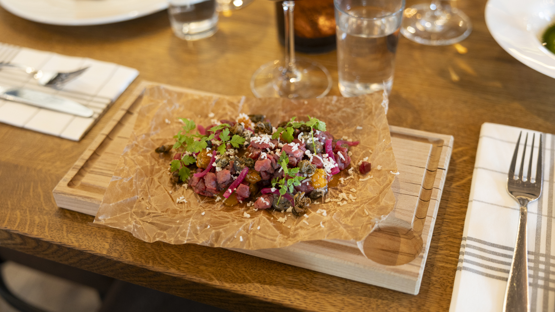 Dekorerad maträtt serverad på träbricka, omgiven av bestick på en restaurang