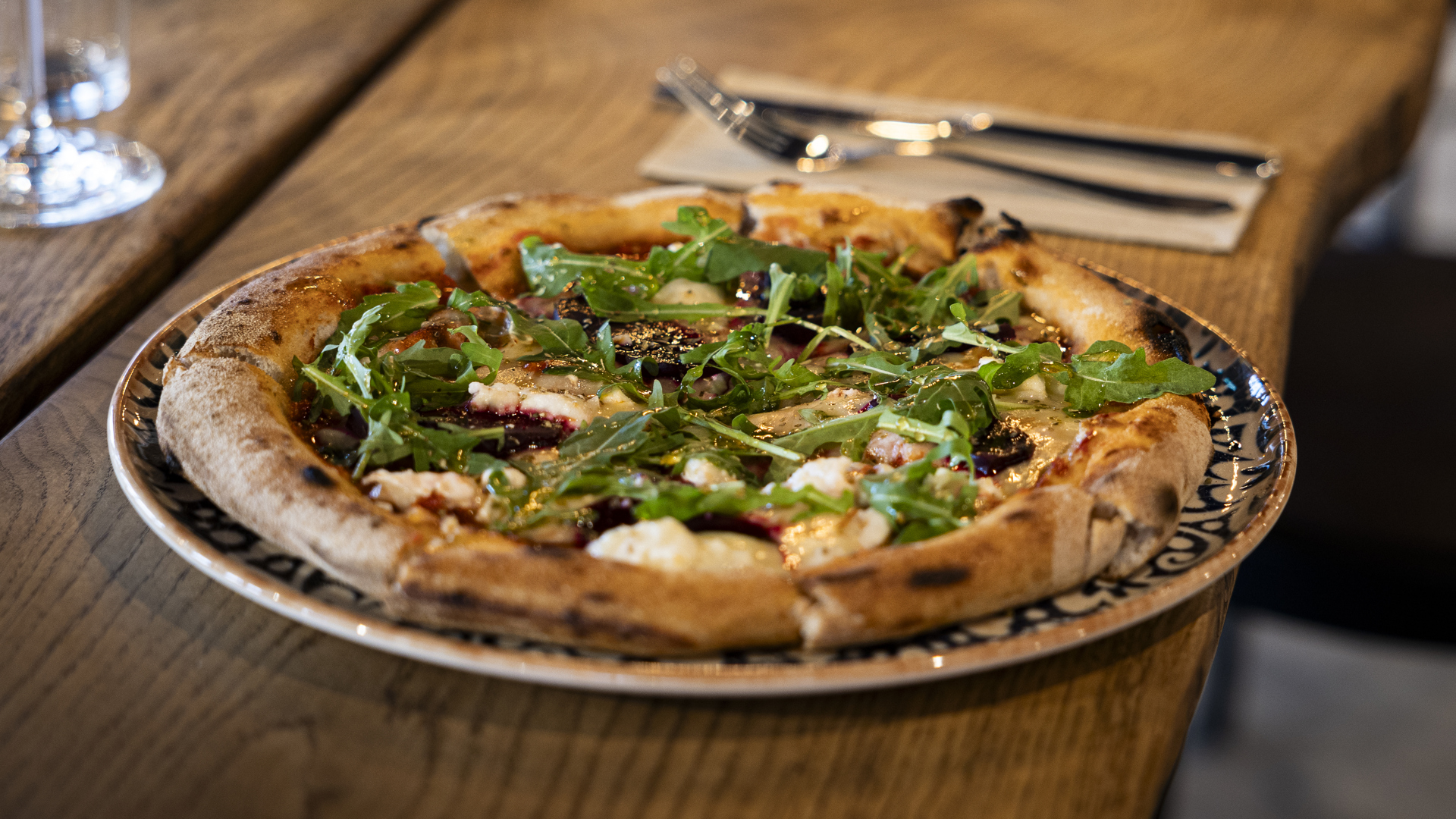 Träbord med en nygräddad pizza toppad med rucola och mozzarella