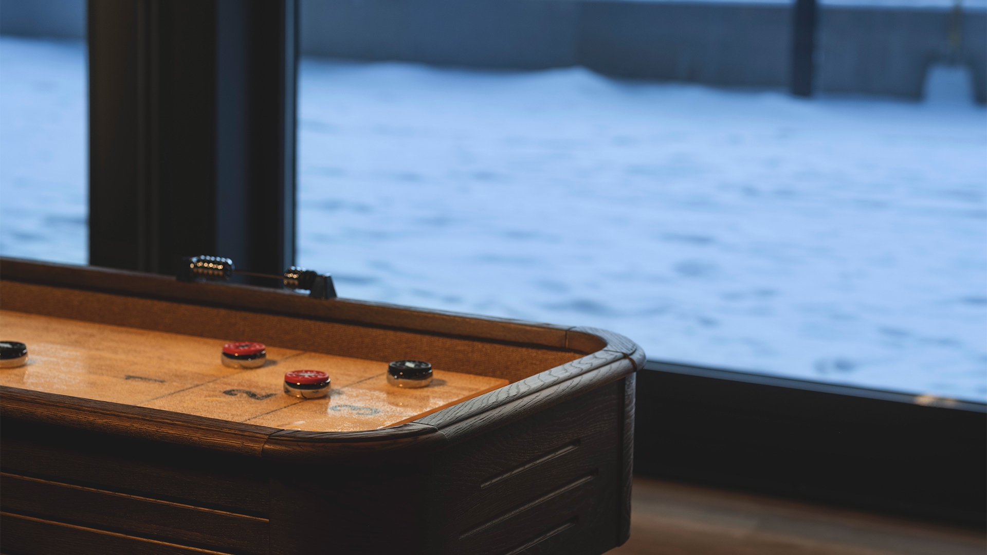 Shuffleboardbord med pjäser vid ett fönster, vinterlandskap utanför
