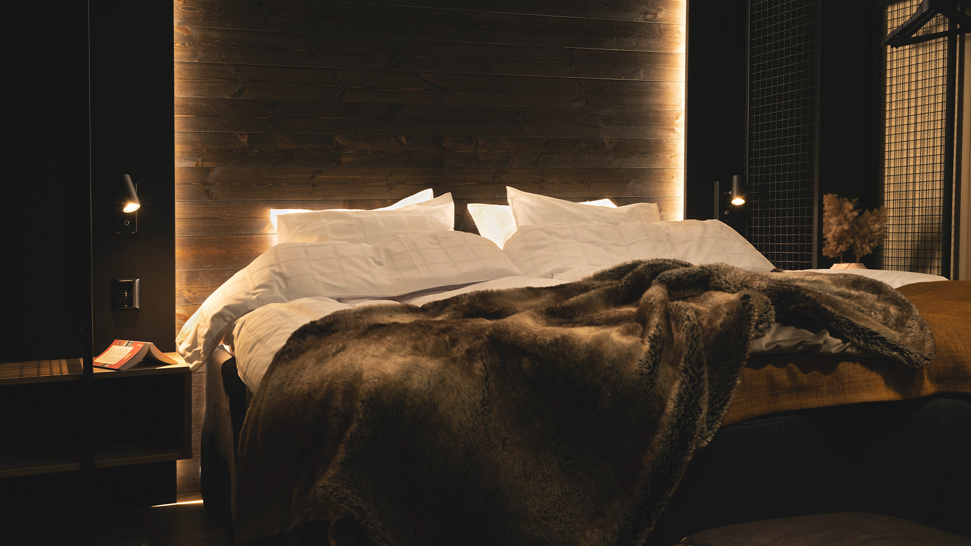 Mysigt sovrum med dubbelsäng och brun filt, omgiven av varm belysning och mörka träväggar