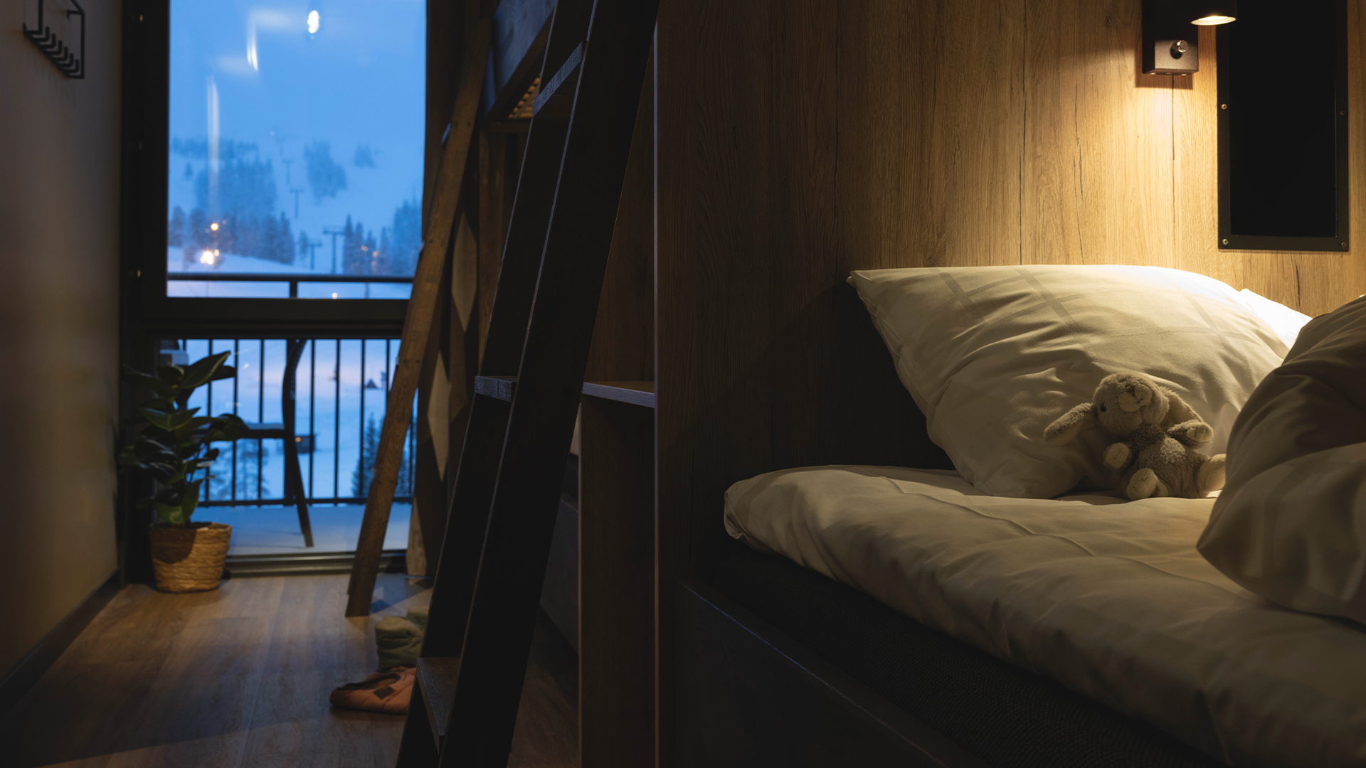 Mysig våningssäng med dämpad belysning, en gosedjurskanin på kudden och vinterlandskap utanför ett fönster i ett modernt rum