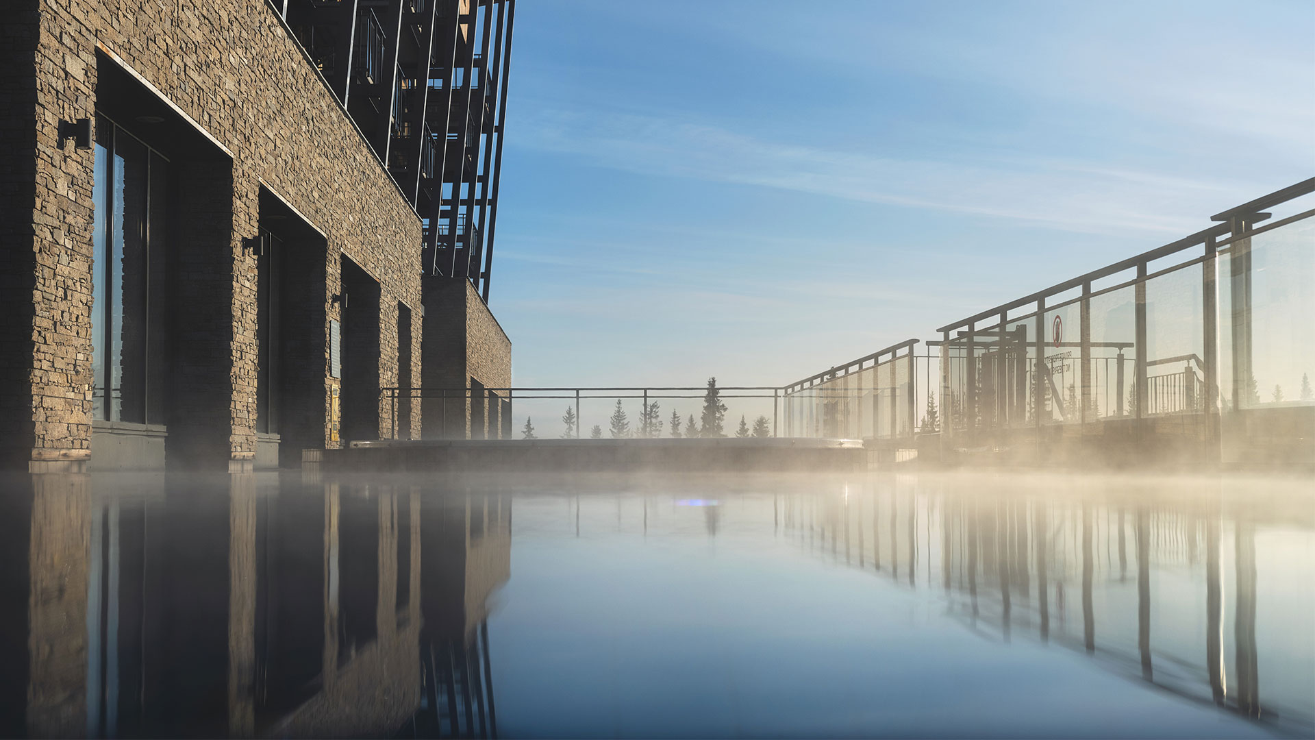 Modern byggnad vid en ångande infinitypool med glasräcke och blå himmel i bakgrunden