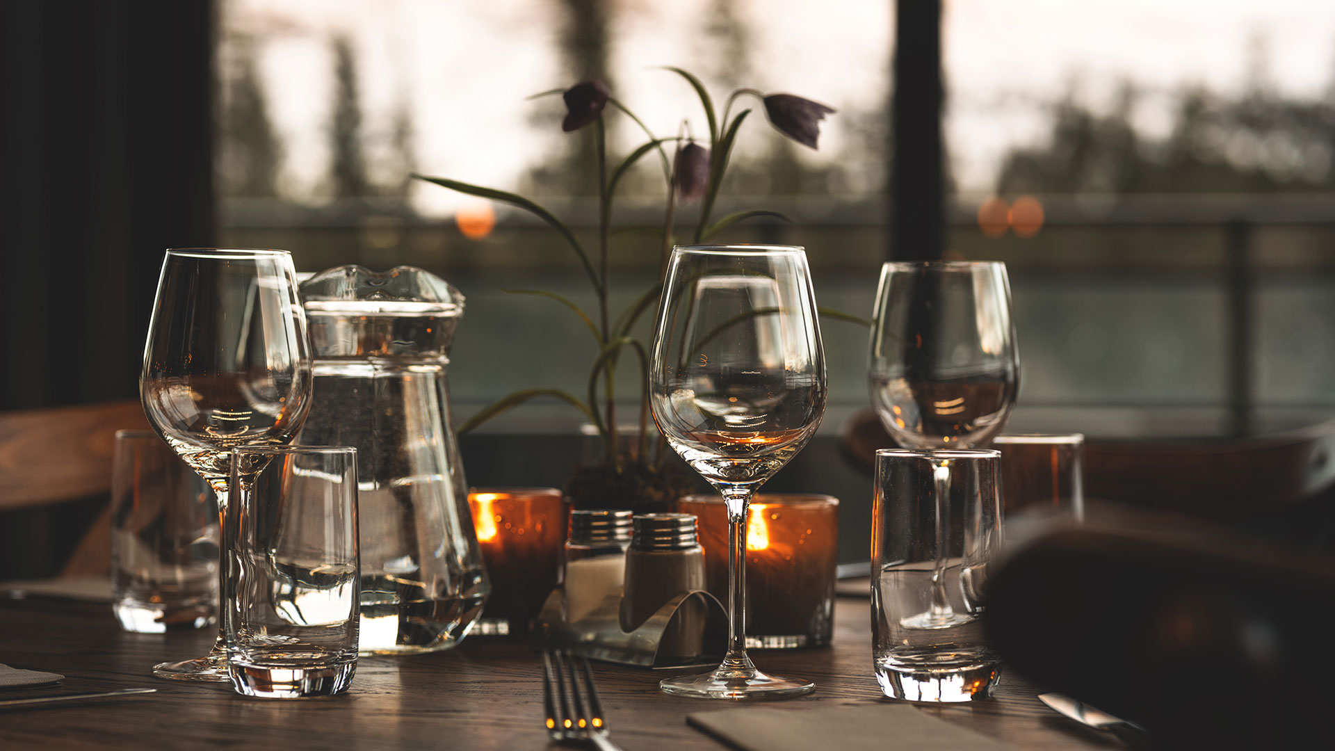Elegant dukning i skymningsljus med vinglas, vattenglas, karaff och levande ljus på restaurangbord