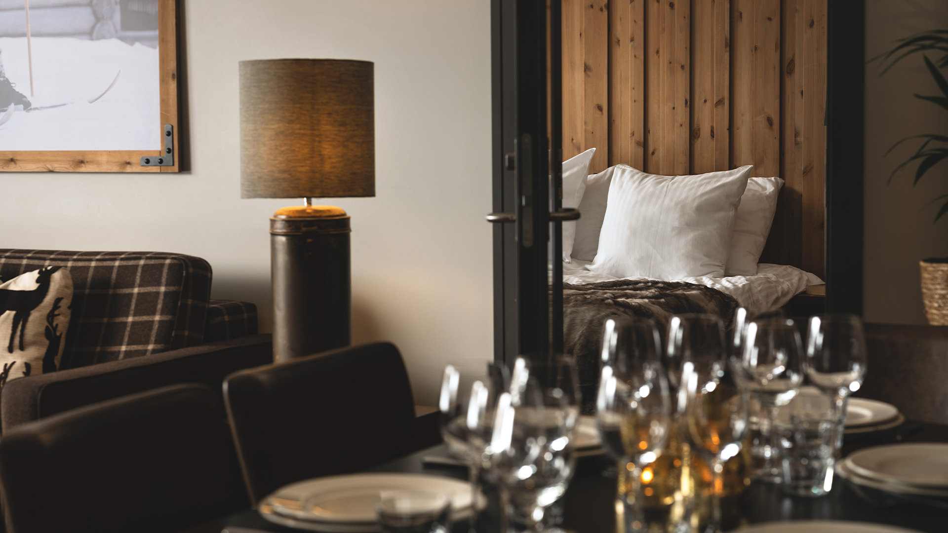 Eleganta hotellinteriörer med dukat bord, mysig soffhörna, lampa och inblick i ett sovrum med träpaneler och vita kuddar