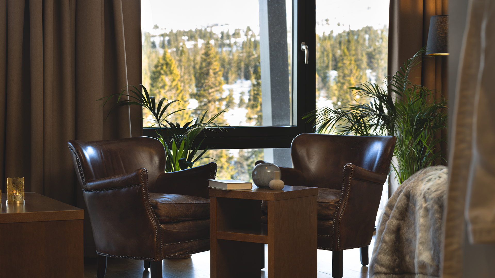 Två bruna läderfåtöljer i ett rum med stort fönster som visar ett vinterlandskap med skog