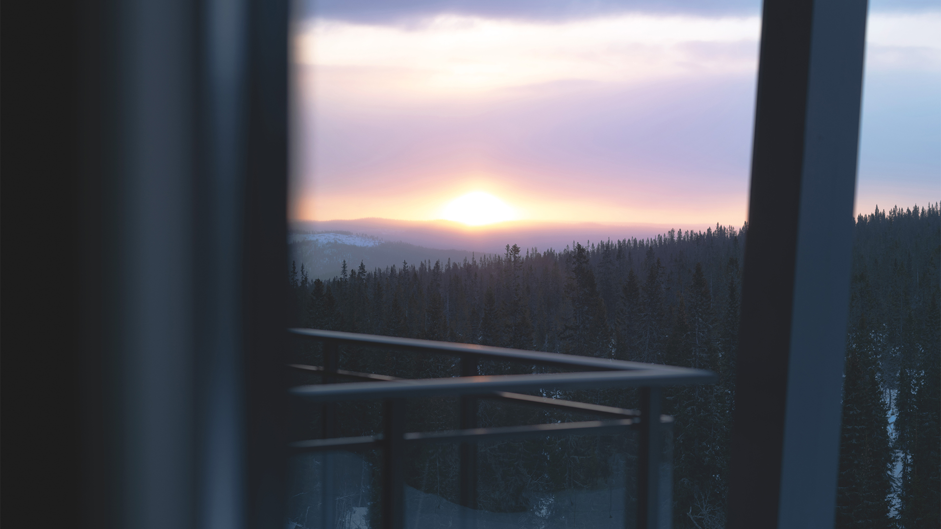 Soluppgång över skogshorisont sedd från en balkong med glasräcke