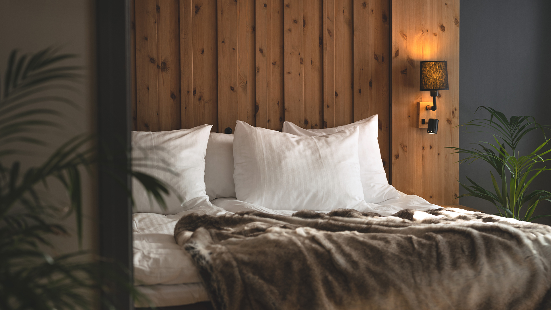 Sovrum med en mysig dubbelsäng, träpanelvägg och dämpad belysning, dekorerad med gröna växter
