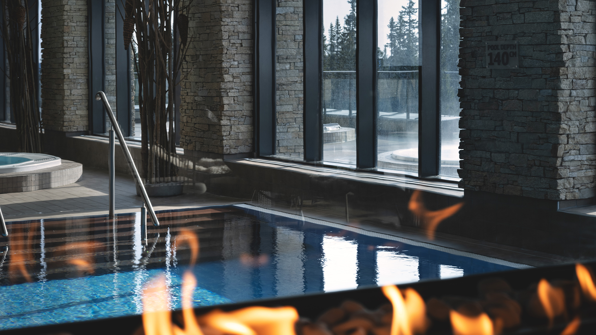 Inomhuspool med stenbeklädda väggar och brinnande eld, med fönster som visar vinterlandskap utanför