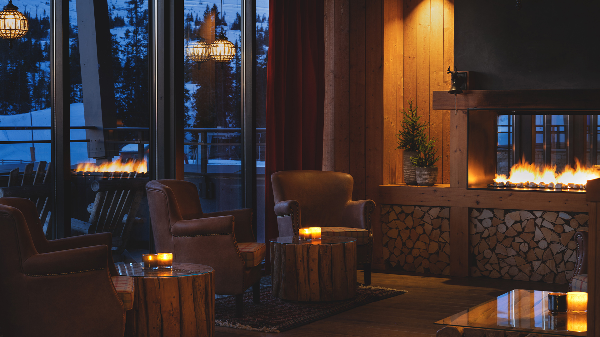 Mysigt vardagsrum med eldstad, läderfåtöljer och utsikt över snöiga landskap genom stora fönster