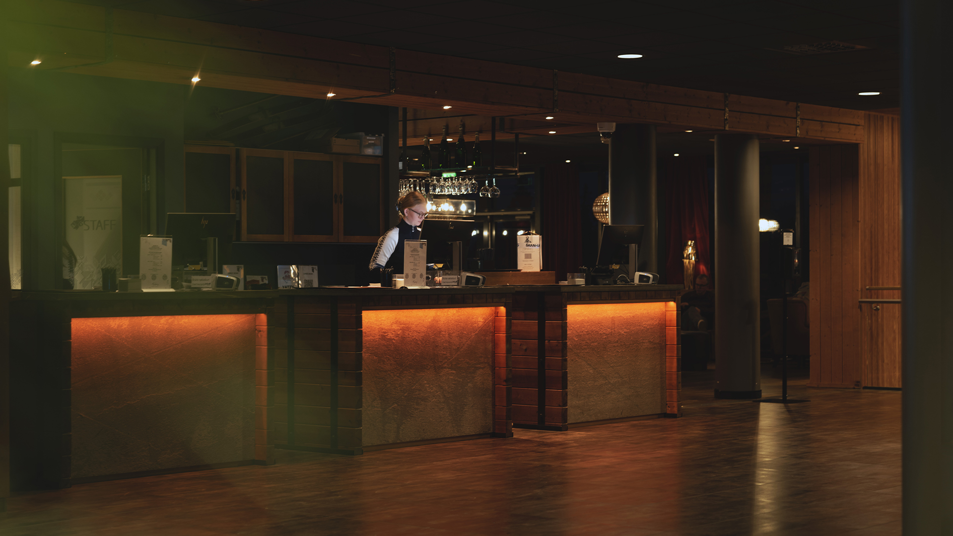 Receptionist vid hotellreception i dämpad belysning, inredning i trä och moderna detaljer