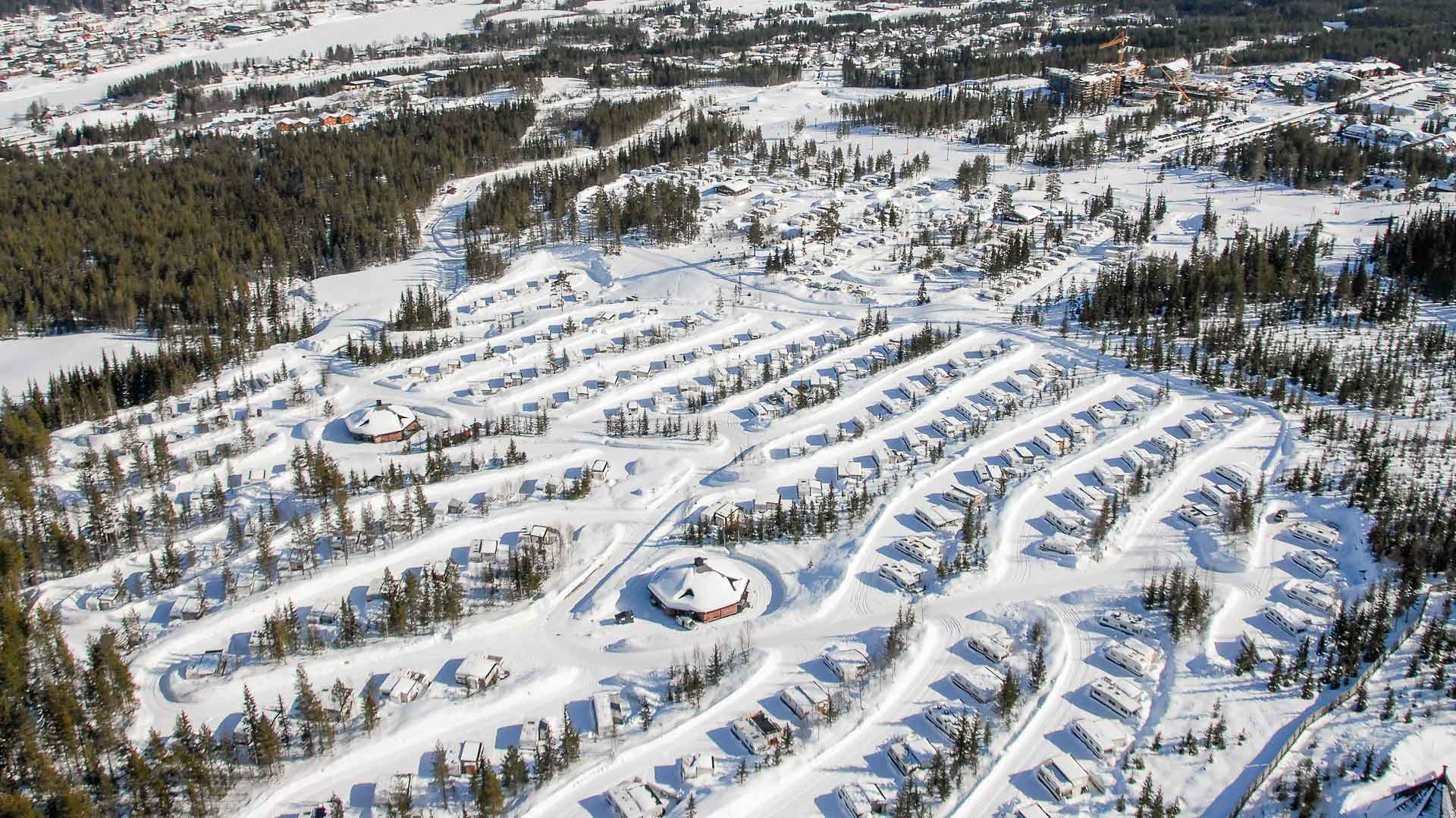 Flygfoto av en vintersportort i fjällen, med snötäckta träd och stugor organiserade i rader
