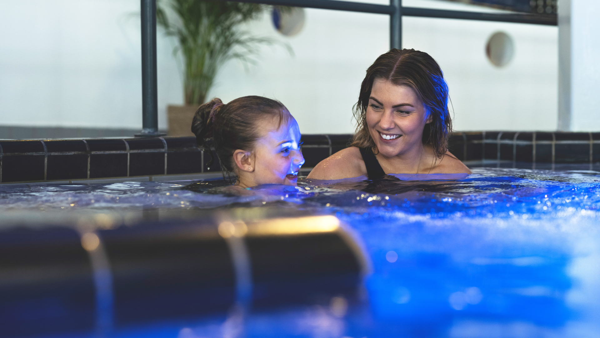 Two women are enjoying a warm bath in a pool with blue lighting
