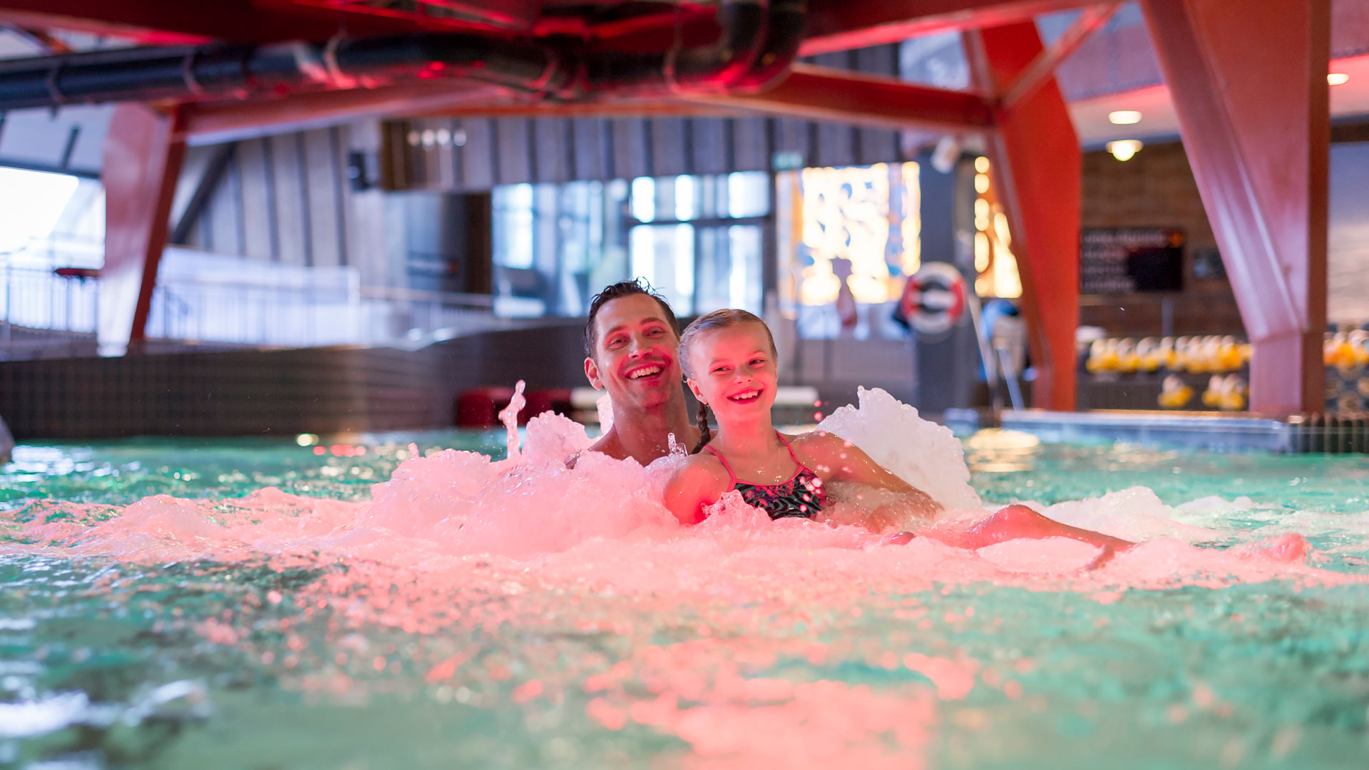 Børn og voksne leger i indendørs swimmingpool med boblevand på eventyrbad i Sverige