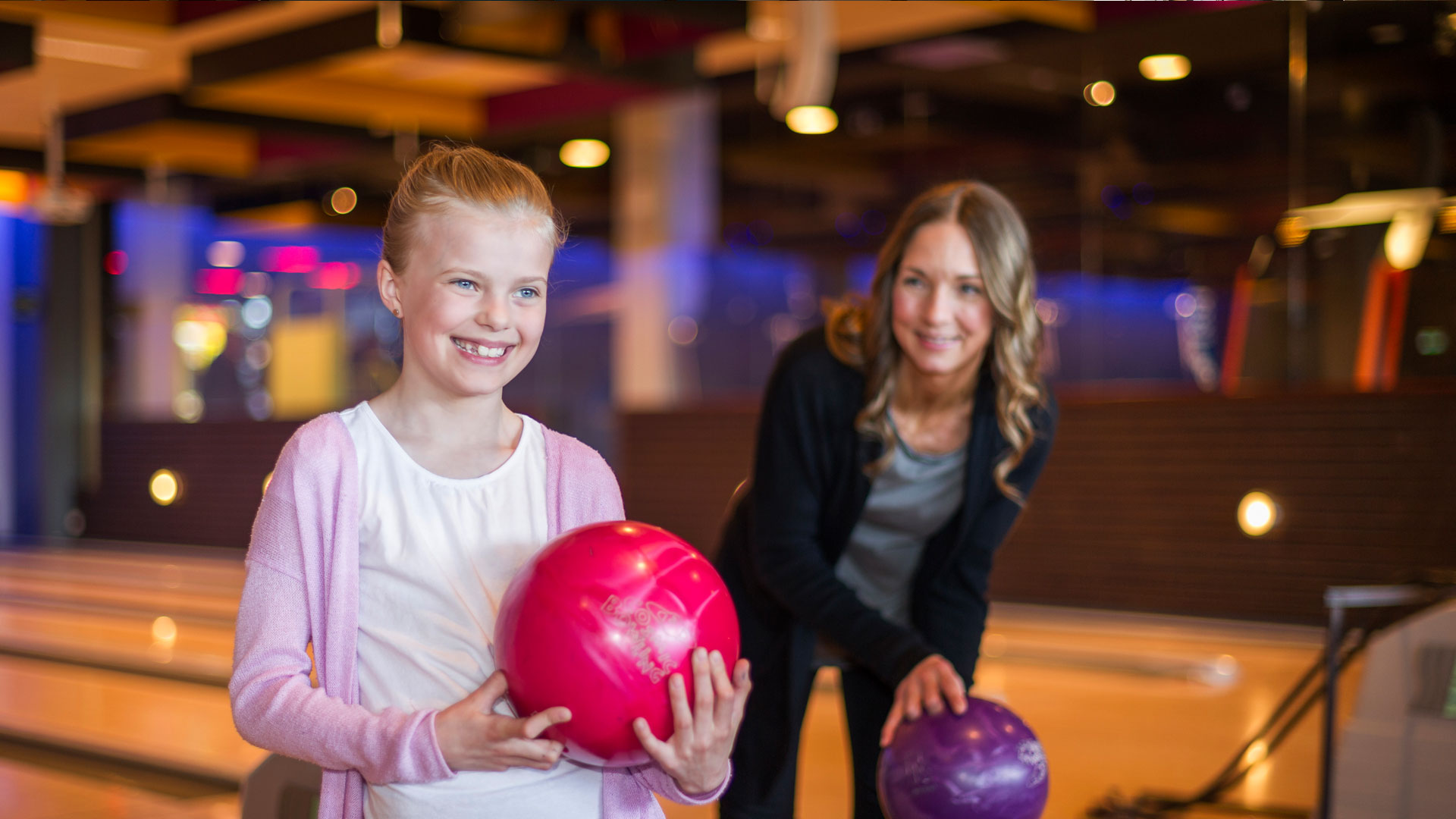 Personer på bowlinghall med färgglada bowlingklot, leende och redo för spel