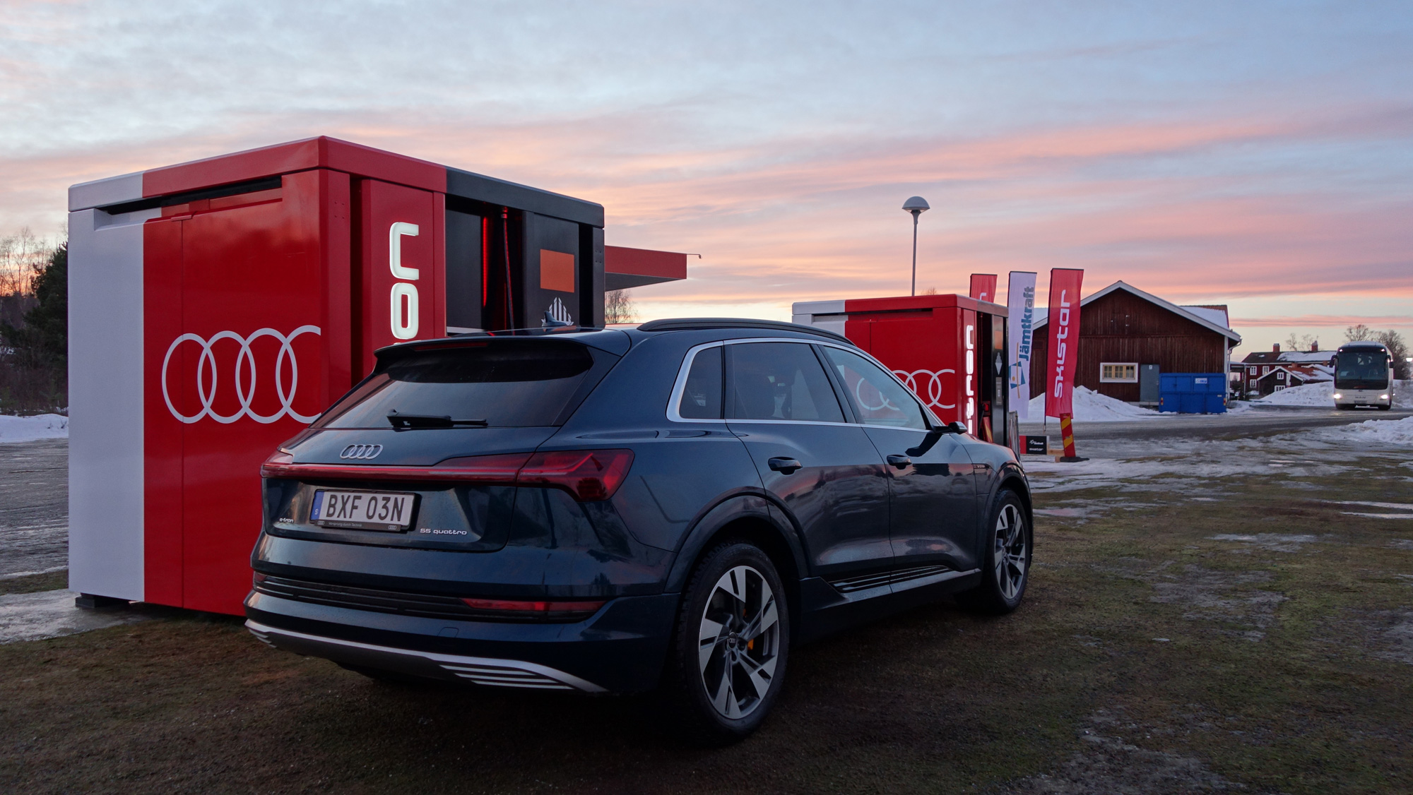 Mörk blå Audi e-tron parkerad vid en laddstation under solnedgången i ett snöigt landskap