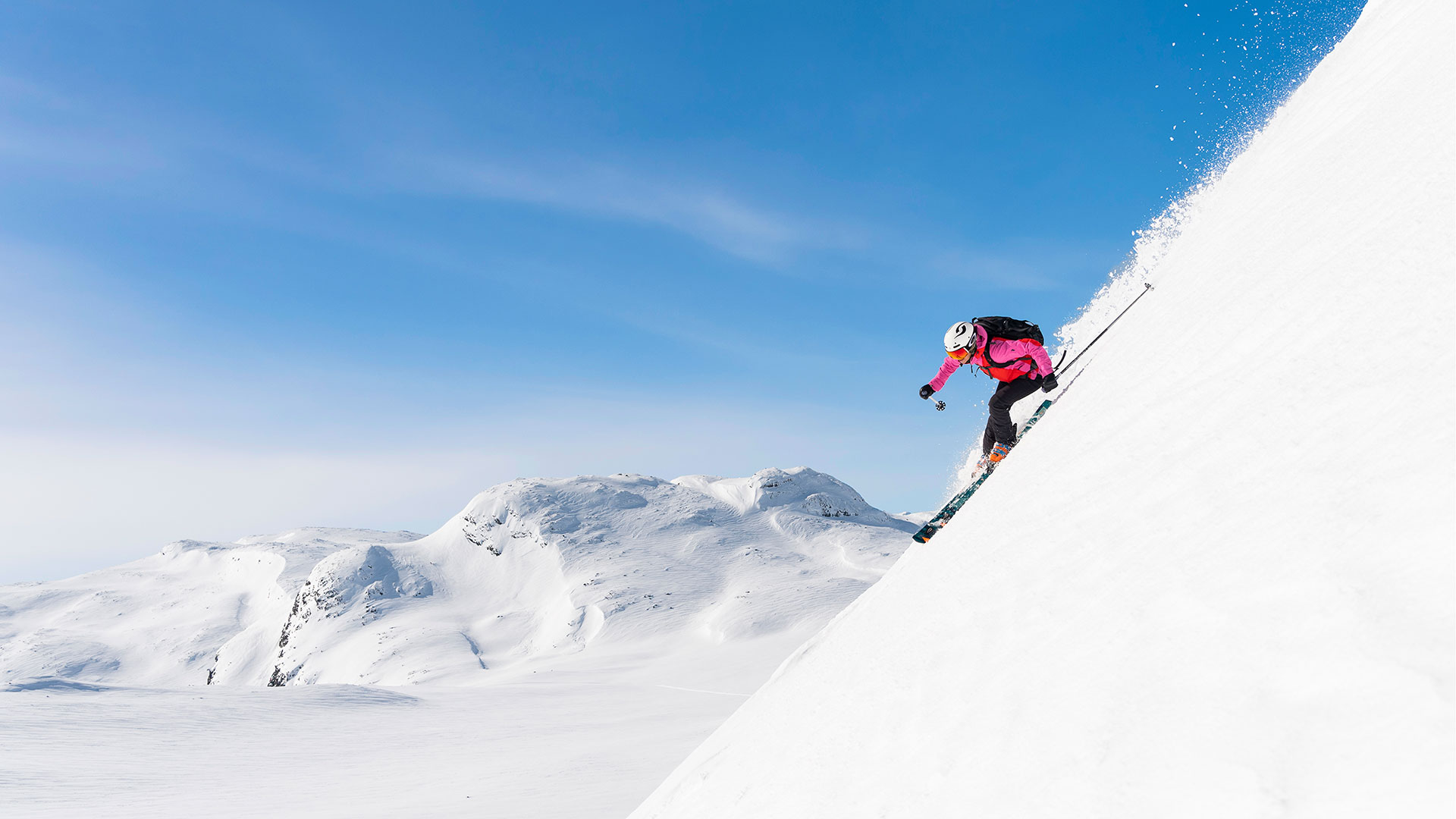 Person som kjører på ski ned en bratt, snødekt fjellskrent under en klar, blå himmel. Perfekte forhold for ekstremsport i vinterlandskap