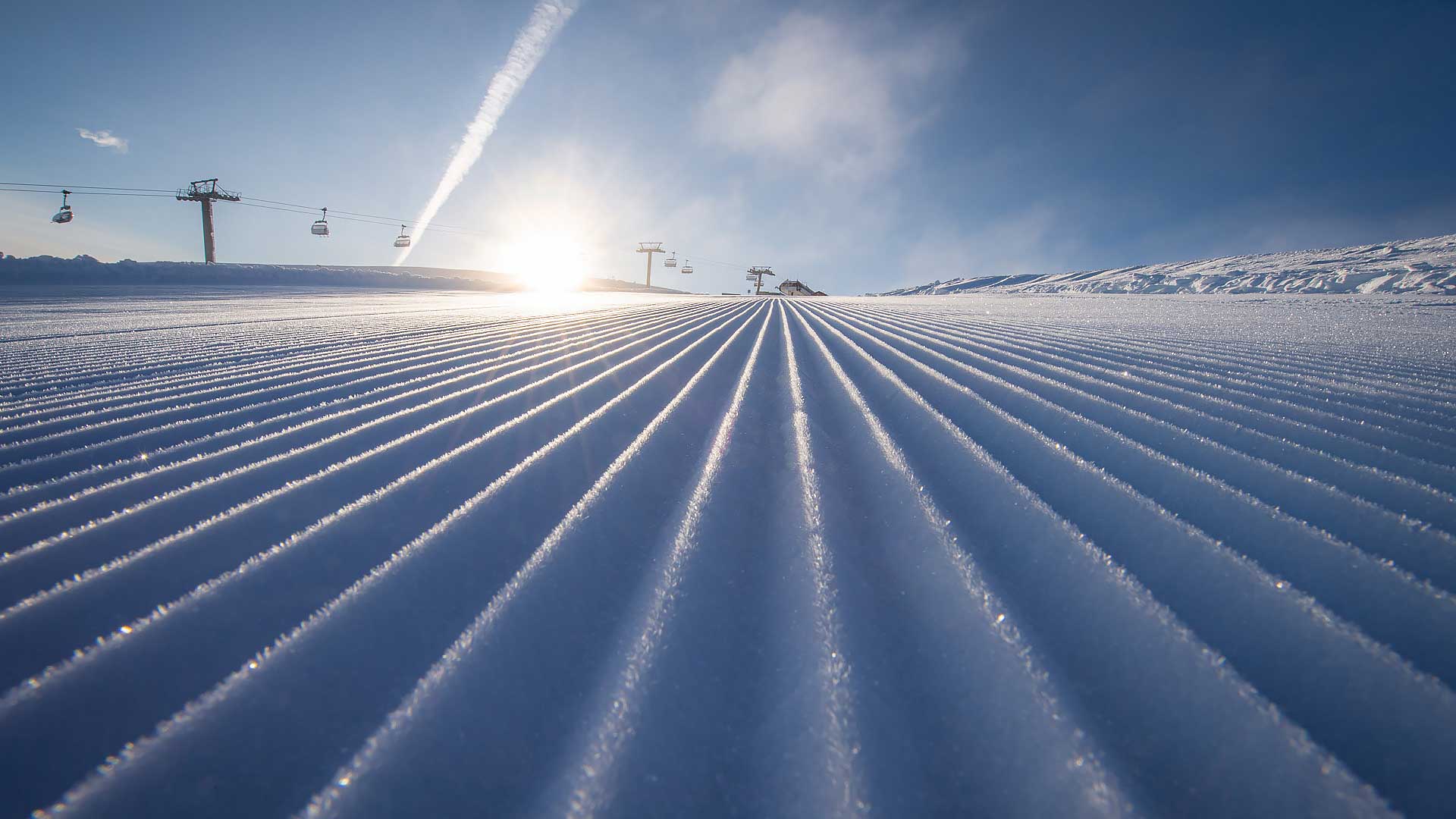 Nypreparert skibakke med soloppgang i bakgrunnen, skiheiser i drift under klar blå himmel