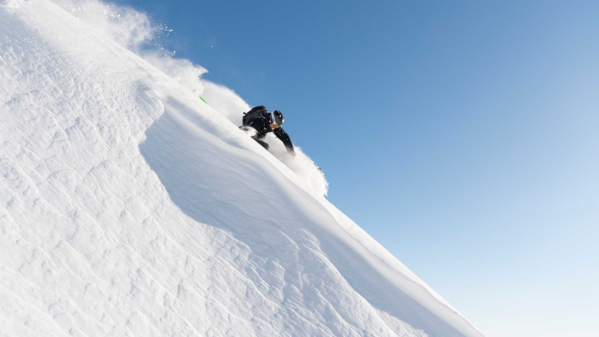 Person som kjører snowboard ned en bratt snødekt bakke under en klar blå himmel