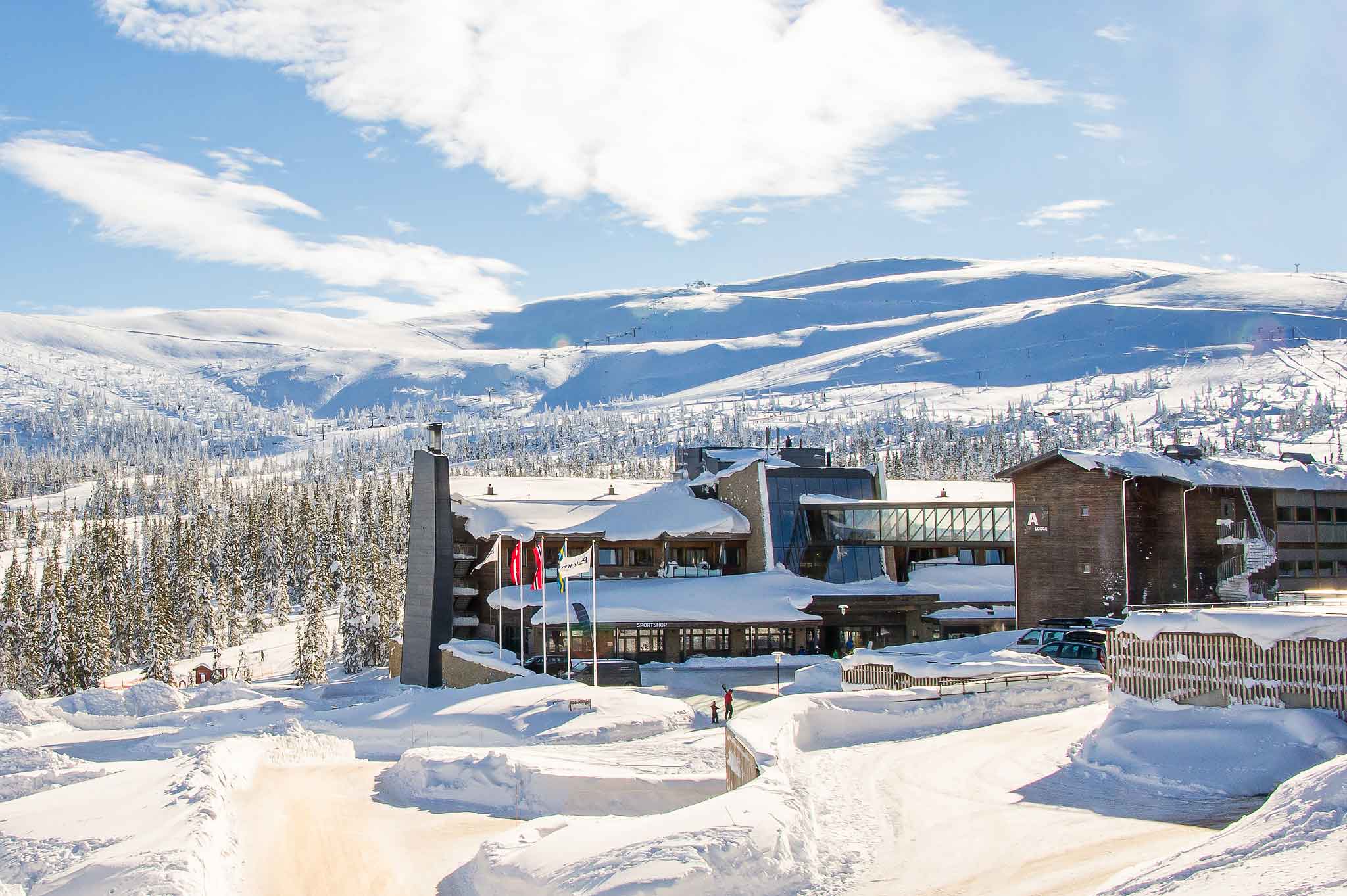 Vinterlandskap med hotell i fjellene, snødekte trær og klare blå himmel i bakgrunnen. Perfekt for ski- og naturentusiaster