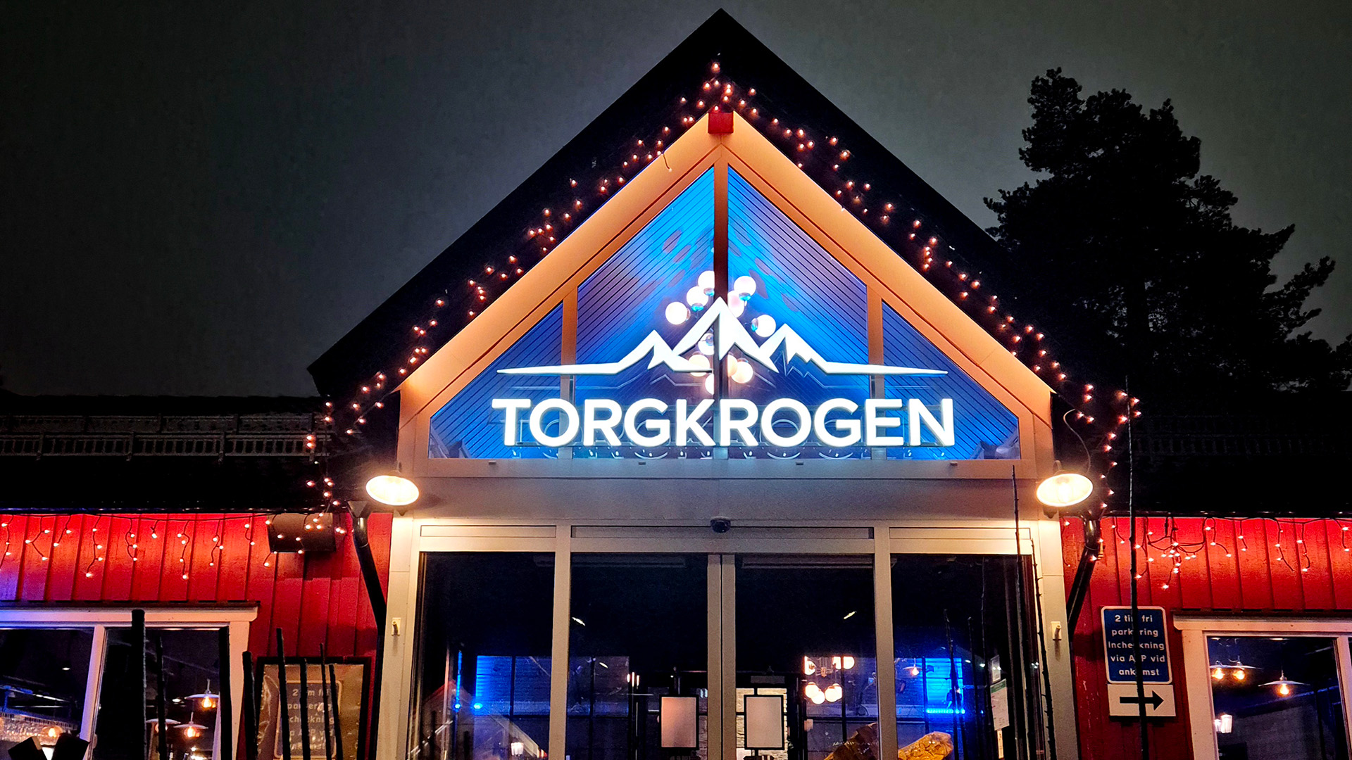 Eingang des Restaurants Torgkrogen mit beleuchteten Lichtern und beleuchtetem Firmenschild in der Nacht.
