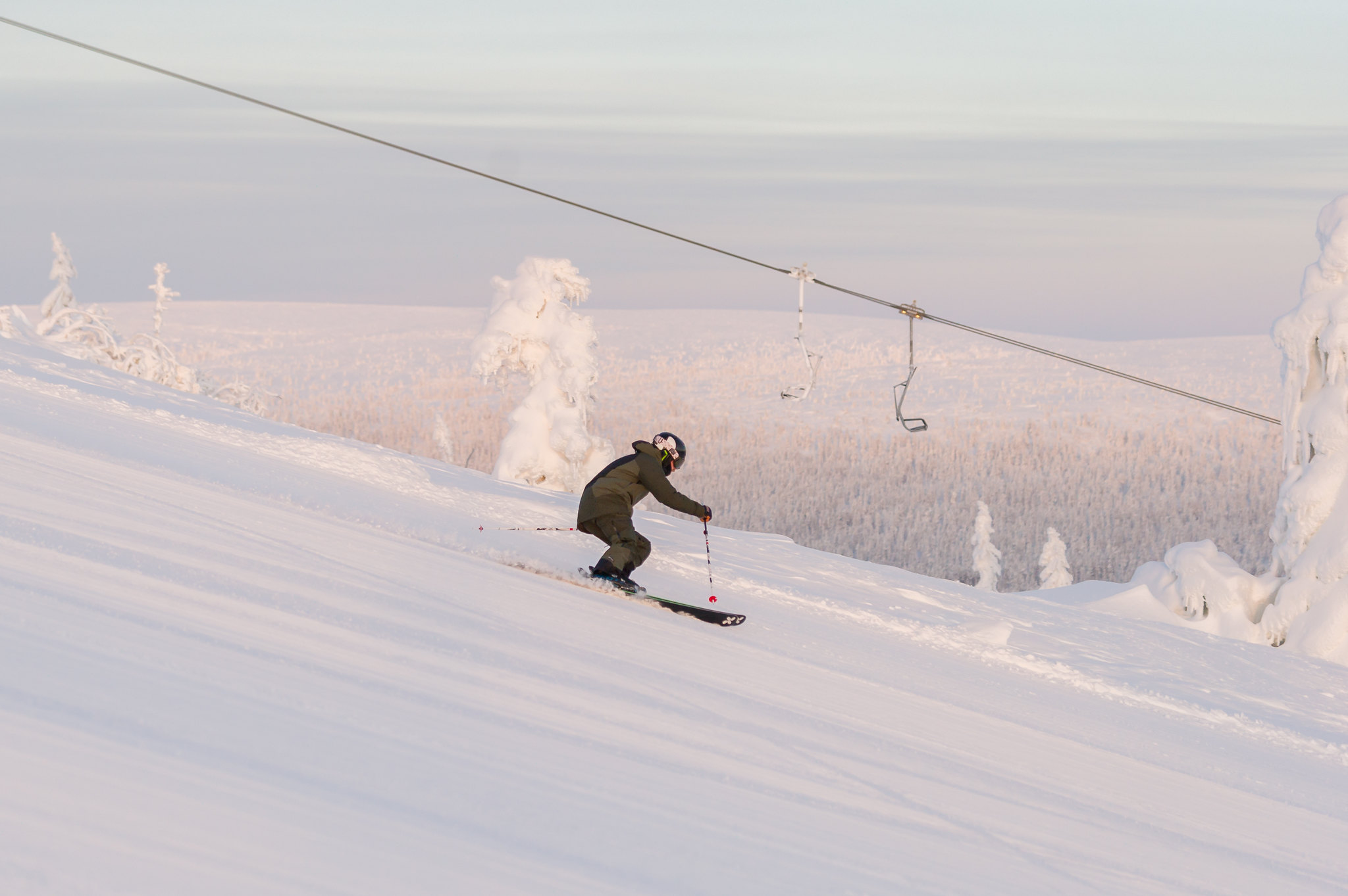 Man åker skidor nerför en snöig backe vid en skidlift, omgiven av vintriga landskap och träden täckta av snö