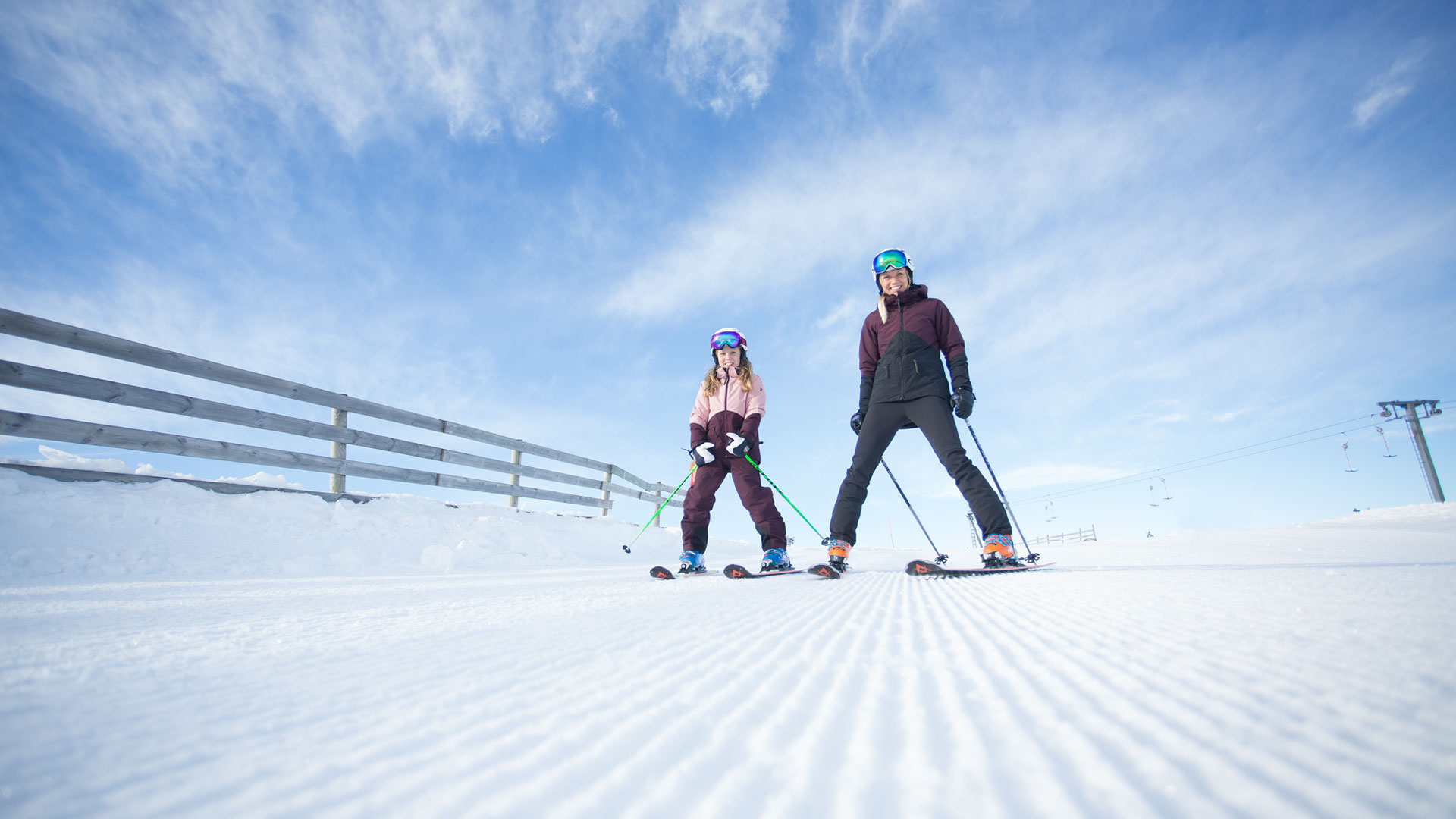 Två personer åker skidor i en solig vintermiljö med klarblå himmel