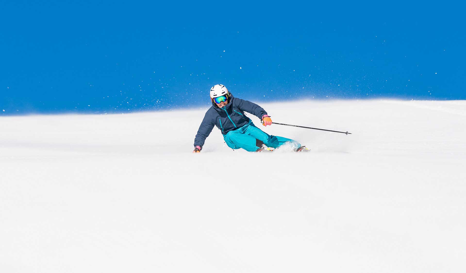A skier in blue equipment is skiing down a white slope against a clear blue sky