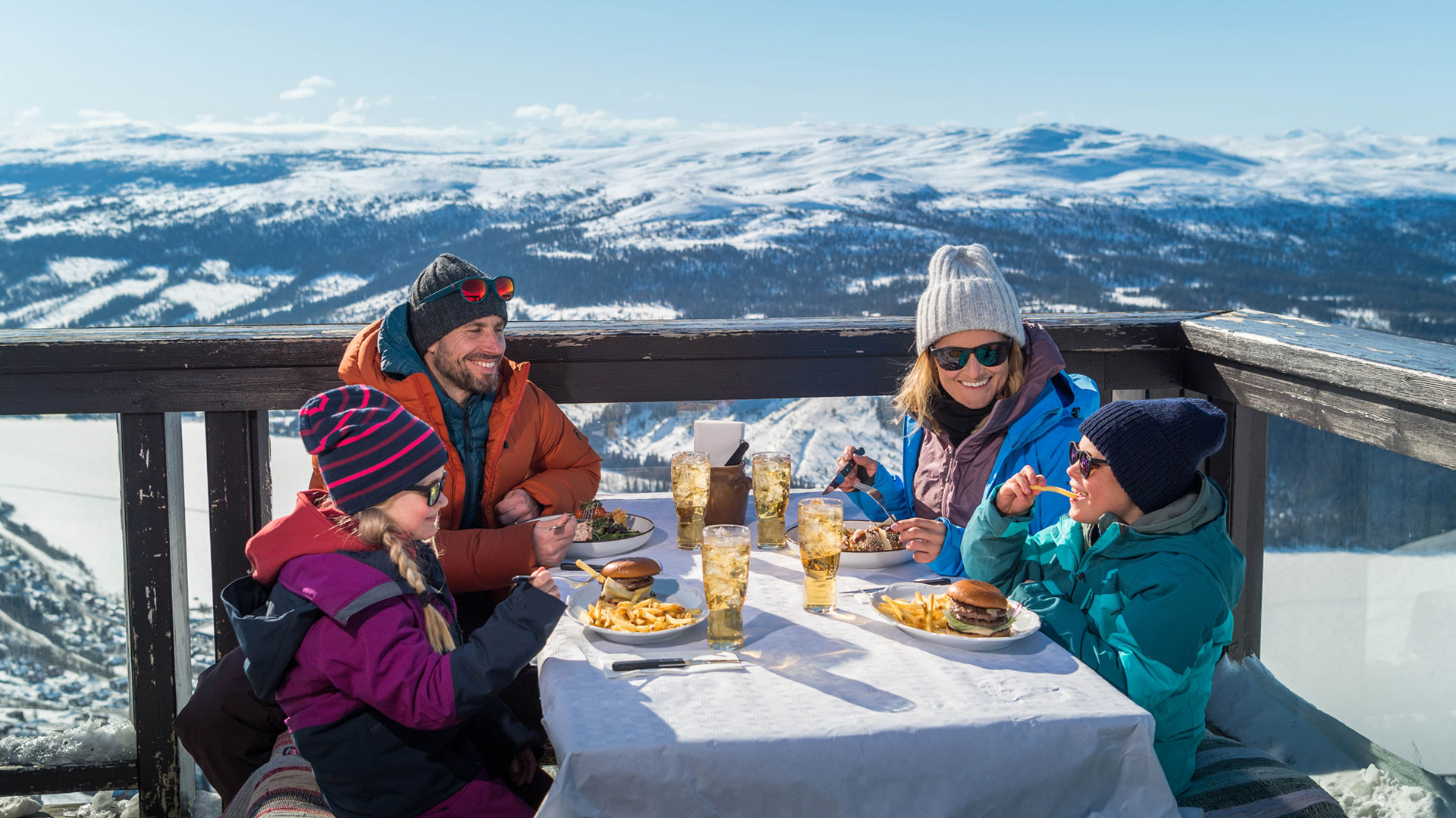 Familj äter lunch på fjällrestaurang med snötäckta berg i bakgrunden, Åre, Sverige