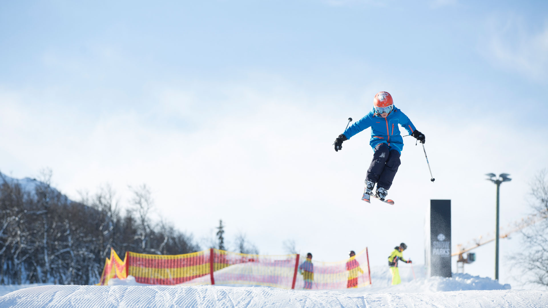 Person som utför ett hopp på skidor i en snöpark med blå himmel i bakgrunden