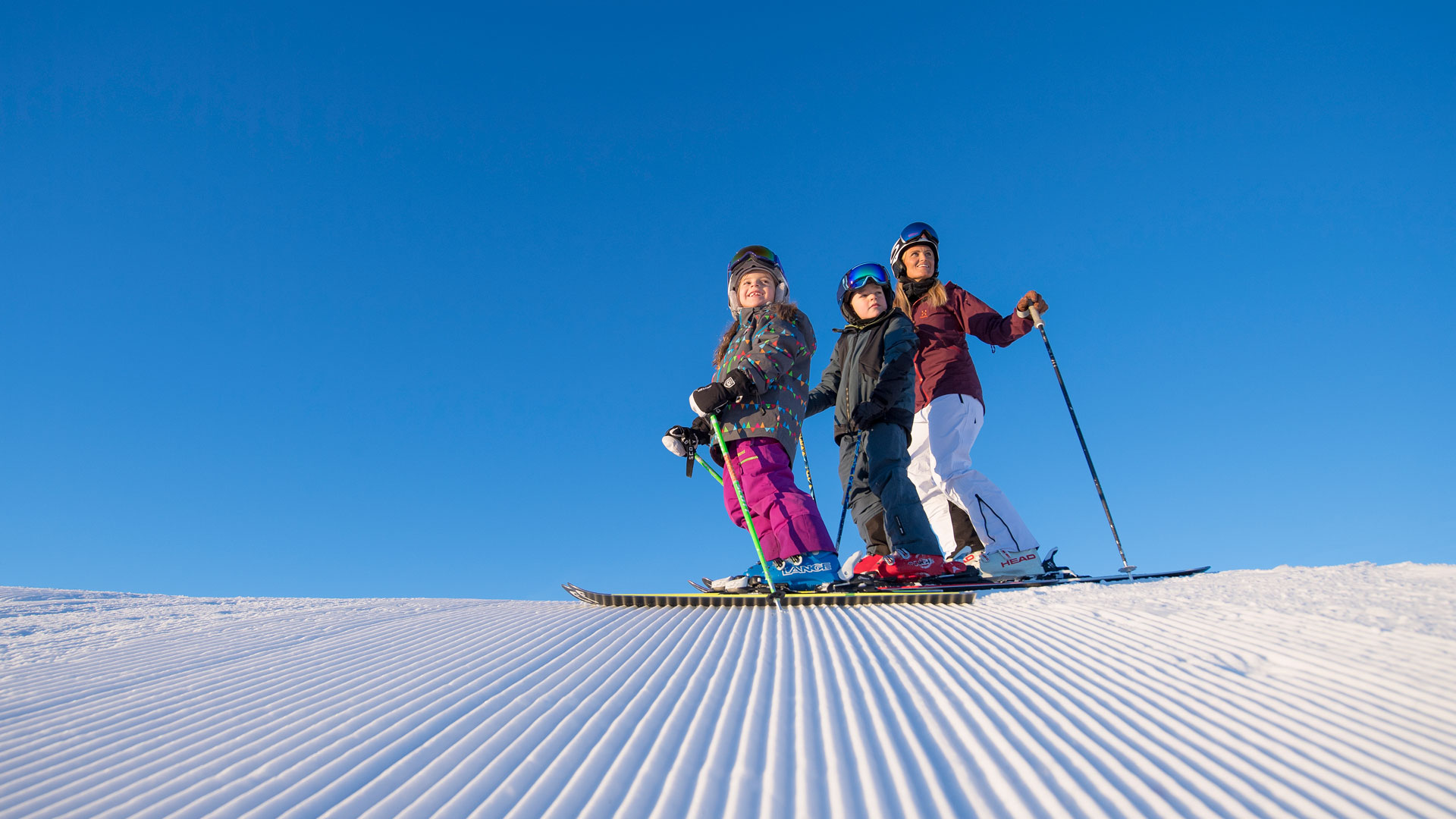 Tre personer åker skidor i soligt väder på en perfekt preparerad skidbacke
