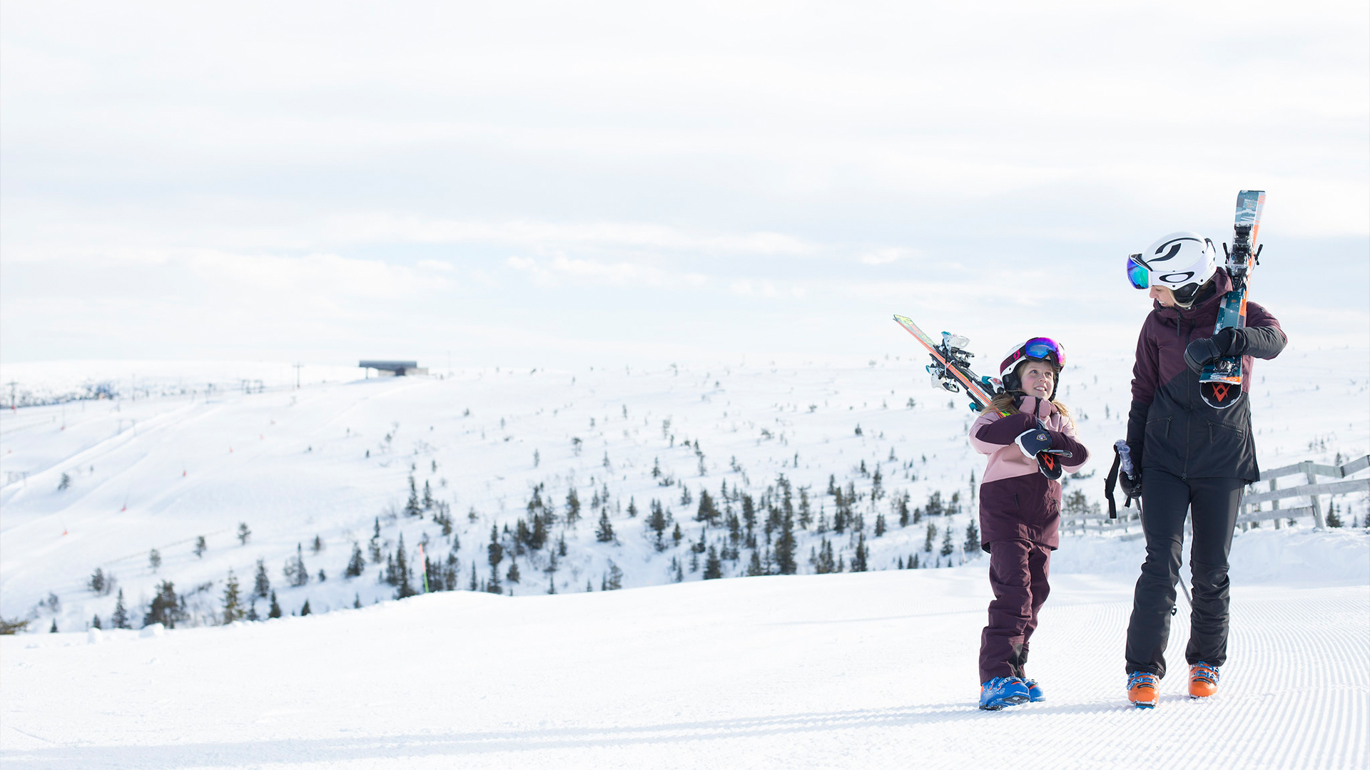 Personer går med skidor på en snöig fjälltopp i ett vintrigt landskap, klädda i skidkläder och hjälmar