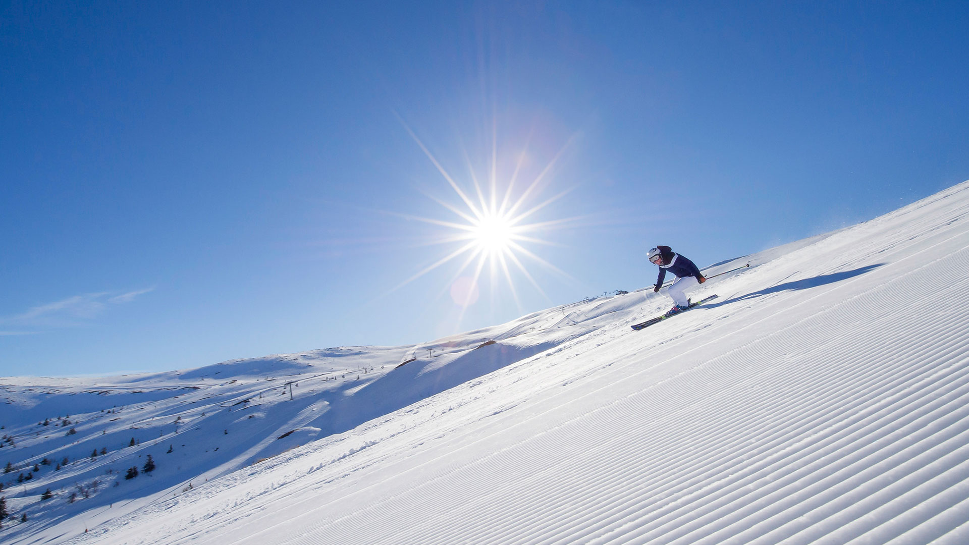 Skiers on a sunny day going down a groomed ski slope in a snowy mountain landscape