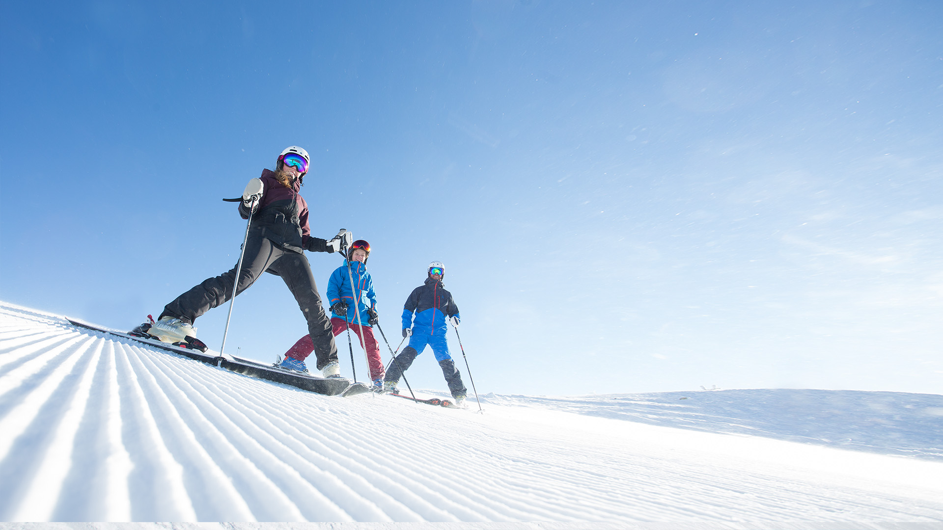 Tre personer åker skidor nedför en skidbacke under en klar och solig vinterdag