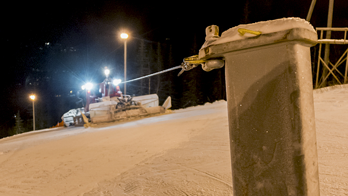 Schneepflug, der in der Nacht Skipisten präpariert, mit starken Lampen, die den schneebedeckten Hang beleuchten