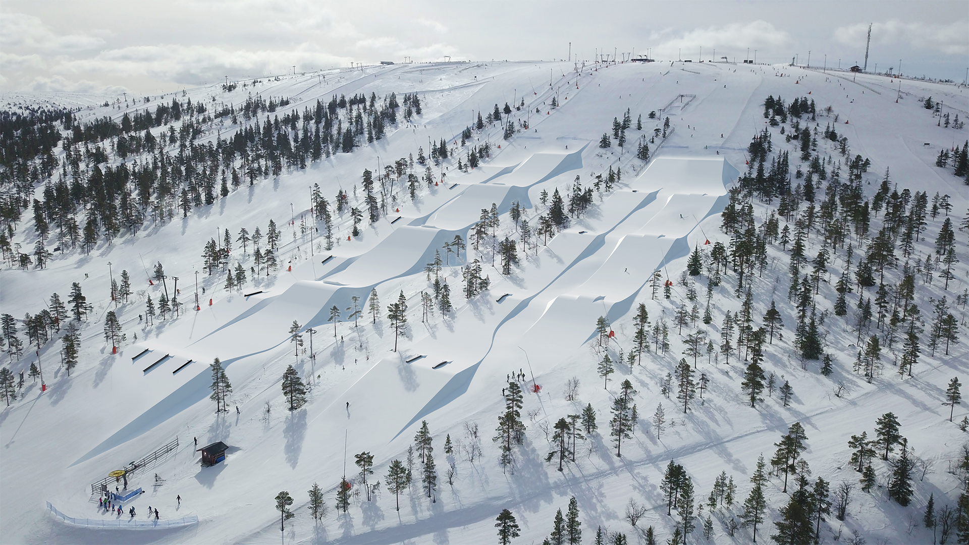 Vinterlandskap med skidbacke och terrängpark omgiven av snöklädda träd i fjällen