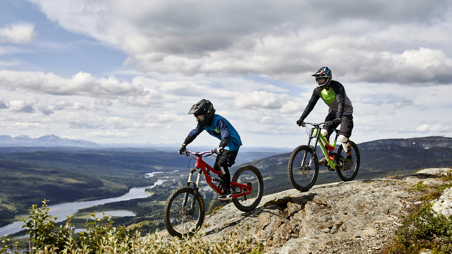 Zwei Mountainbikefahrer fahren auf einem Bergweg mit Panoramablick über das Tal in Åre, Schweden, unter einem bewölkten Himmel