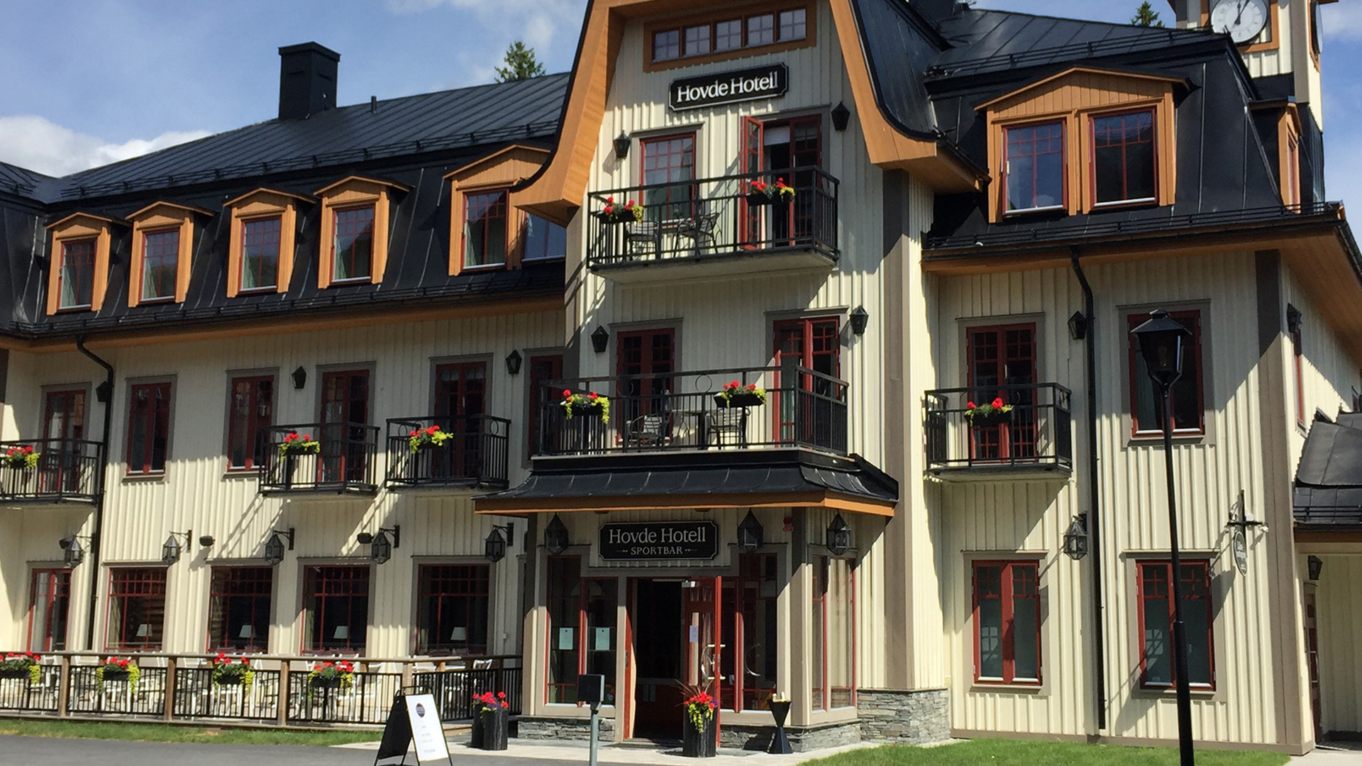 Hovde Hotell fasad i fjällmiljö, modern byggnad med traditionell svensk arkitektur och dekorerade balkonger, solsken och blå himmel