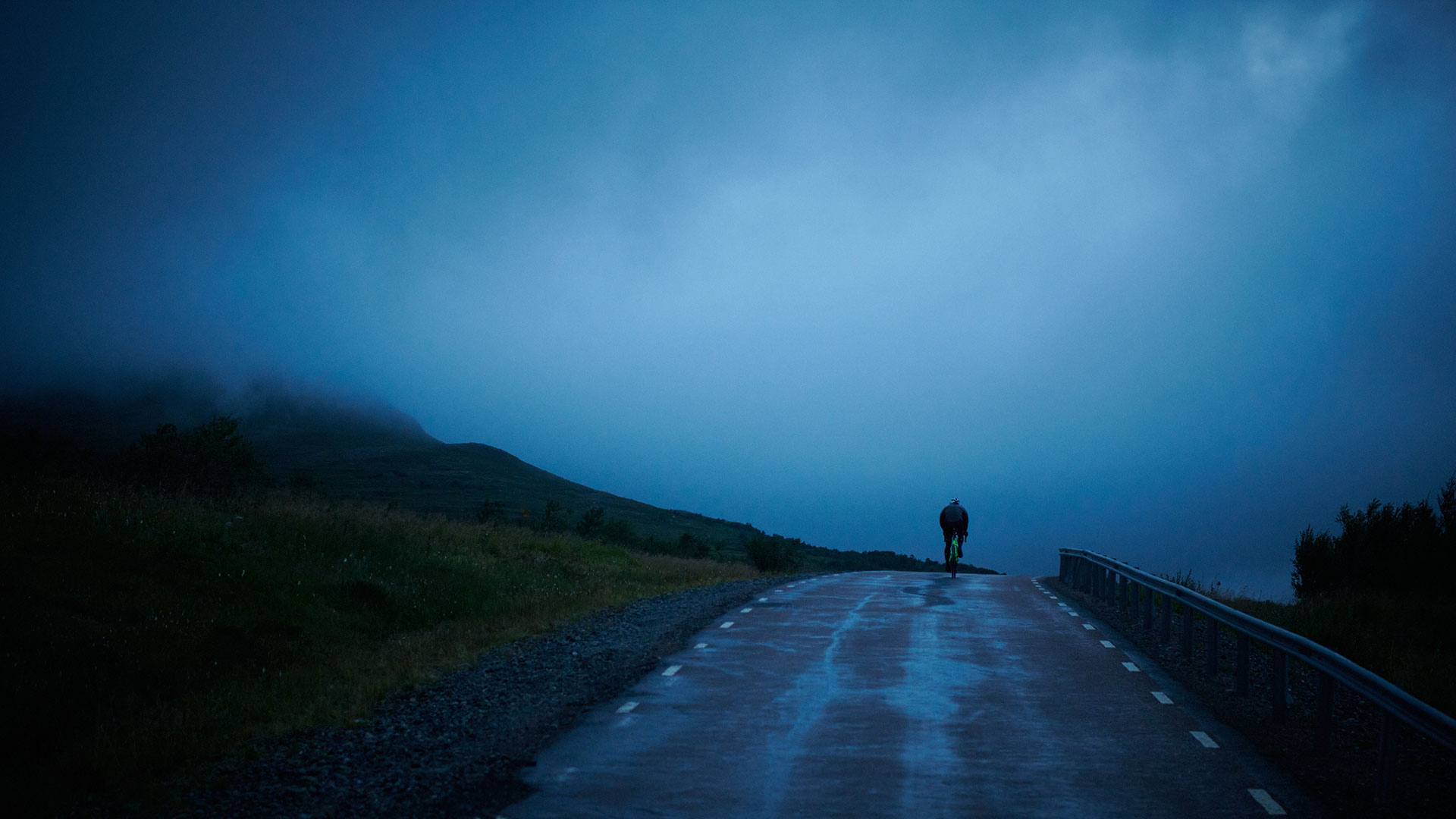 Cyklist på regnig väg mot dimmig horisont i skymning