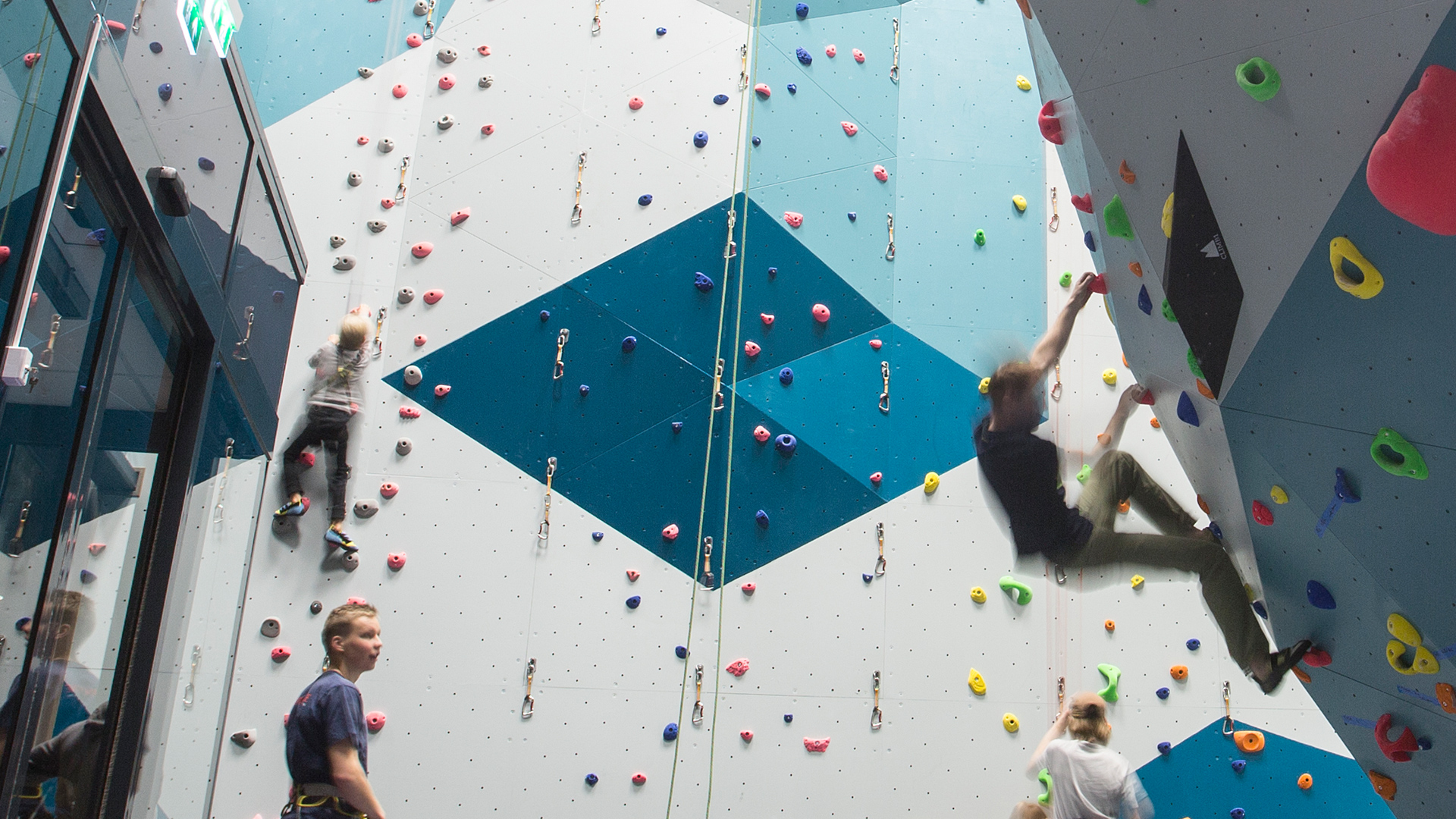 Indoor climbing in a climbing gym with multiple people on walls featuring various colorful climbing routes