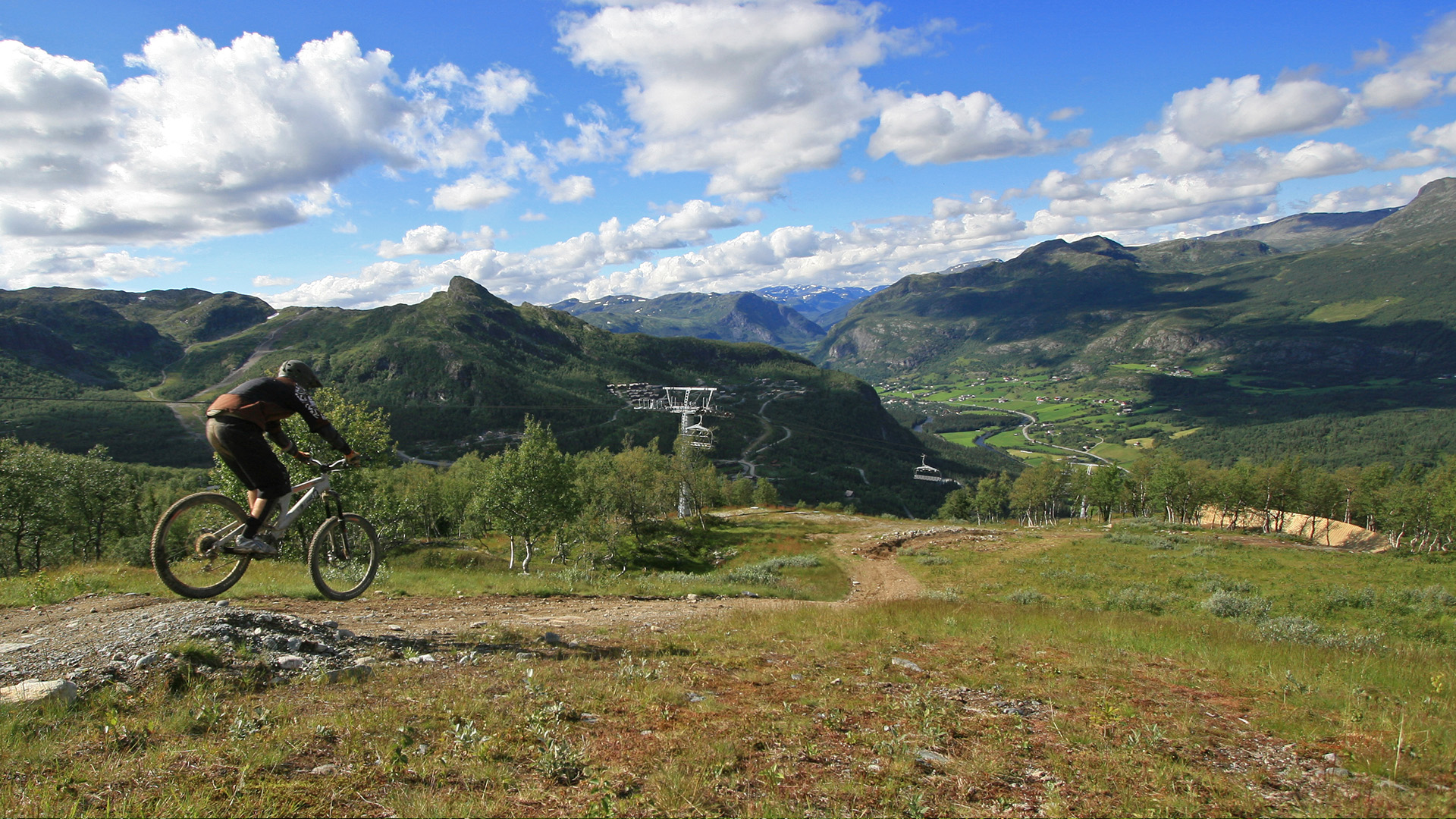 Mountainbike-entusiast åker nedför en stig i en naturskön dal omgiven av berg under en klarblå himmel