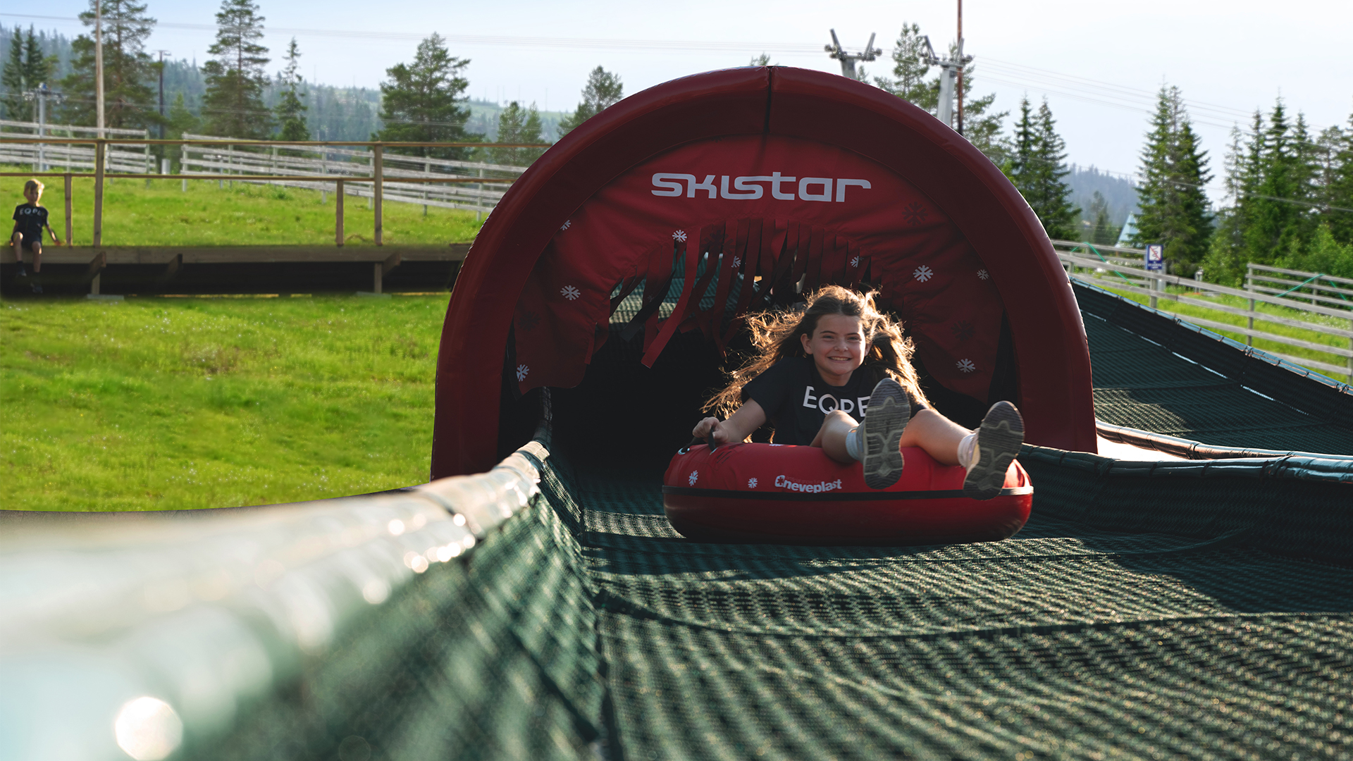 Barn åker i en röd åkring på Skistar-attraktion i en grönskande sommarlandskap med träd i bakgrunden