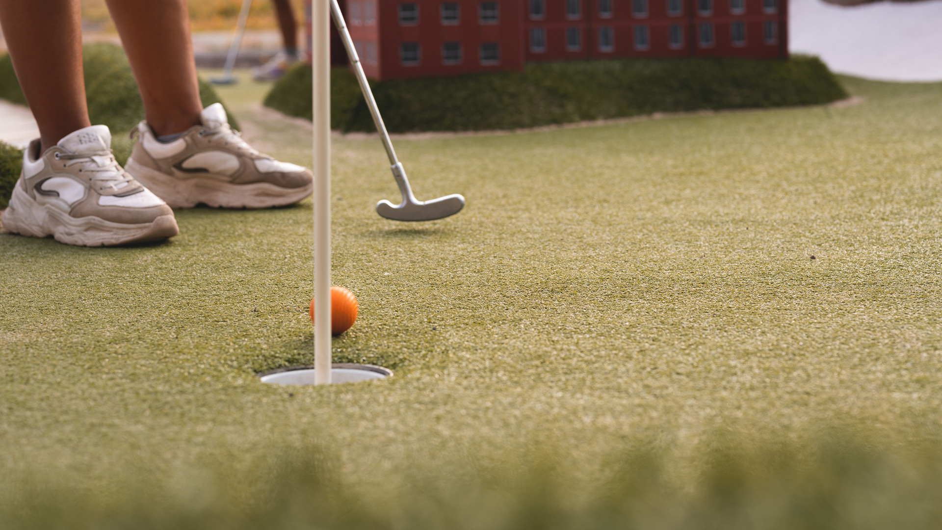 Minigolfspelare siktar och puttar en orange boll mot hålet på en grön och välskött bana
