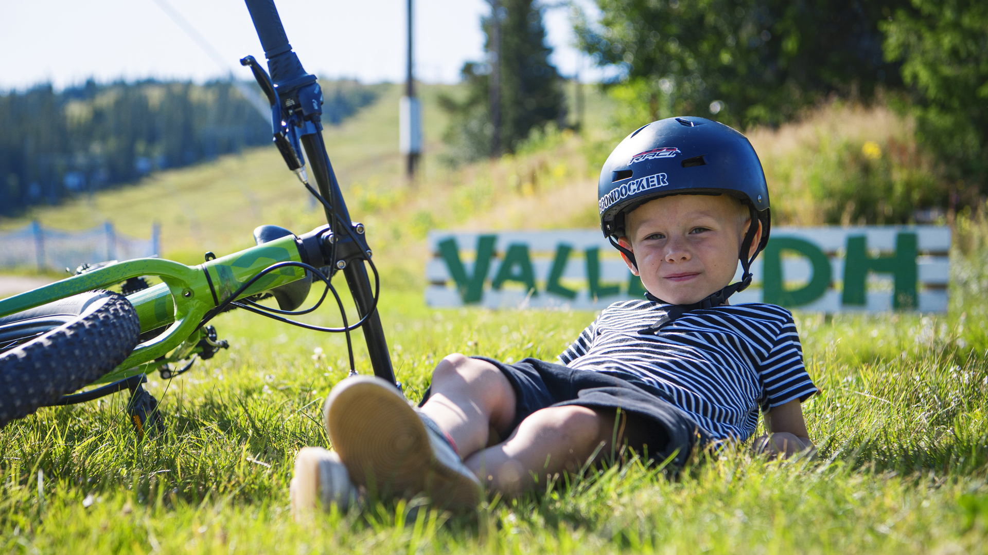 Barn med cykelhjelm hviler ved siden af mountainbike i sommerlig natur i Sverige