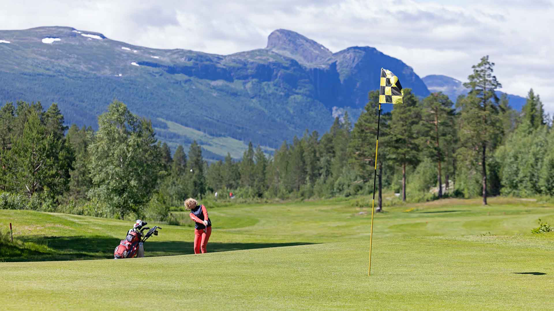 Golfspelare på grön golfbana med berg och skog i bakgrunden i Sverige