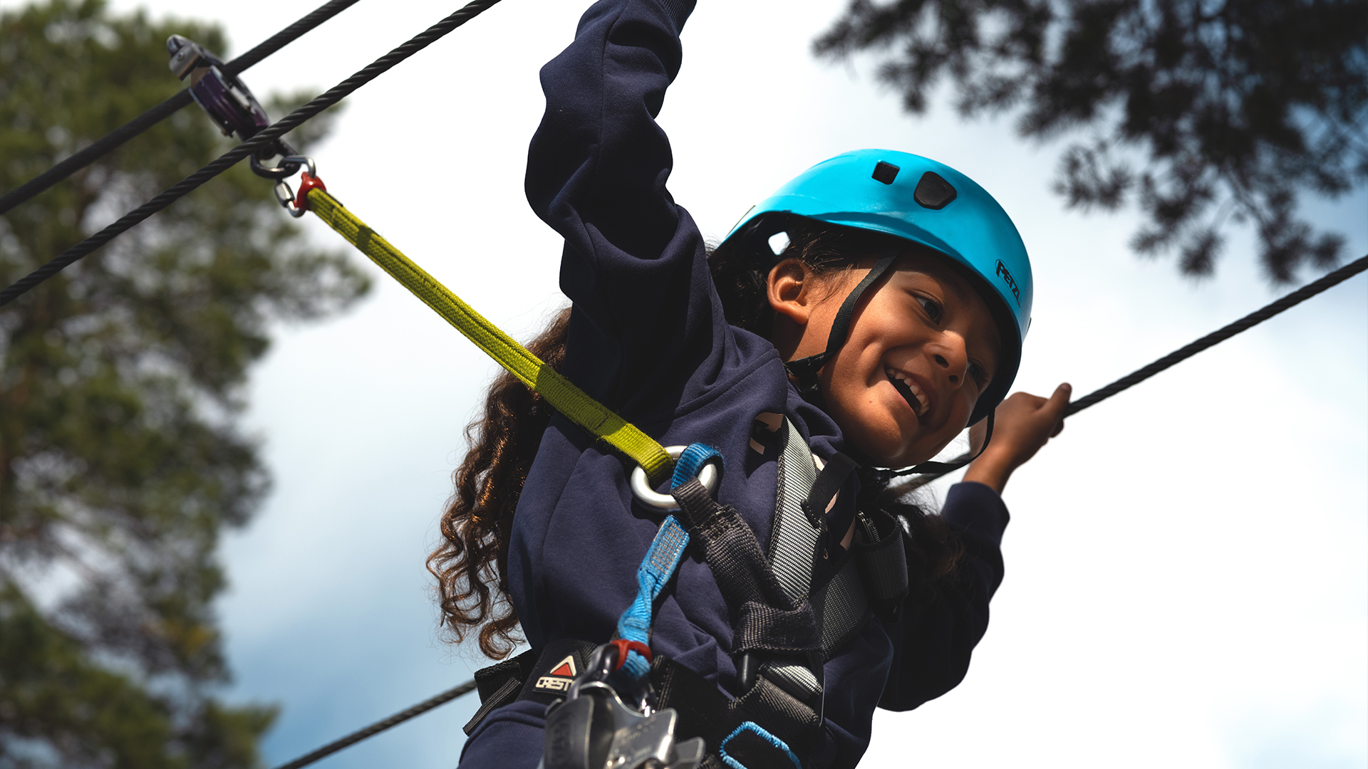 Children in safety gear enjoy a high-altitude course with a harness and helmet in a forest setting