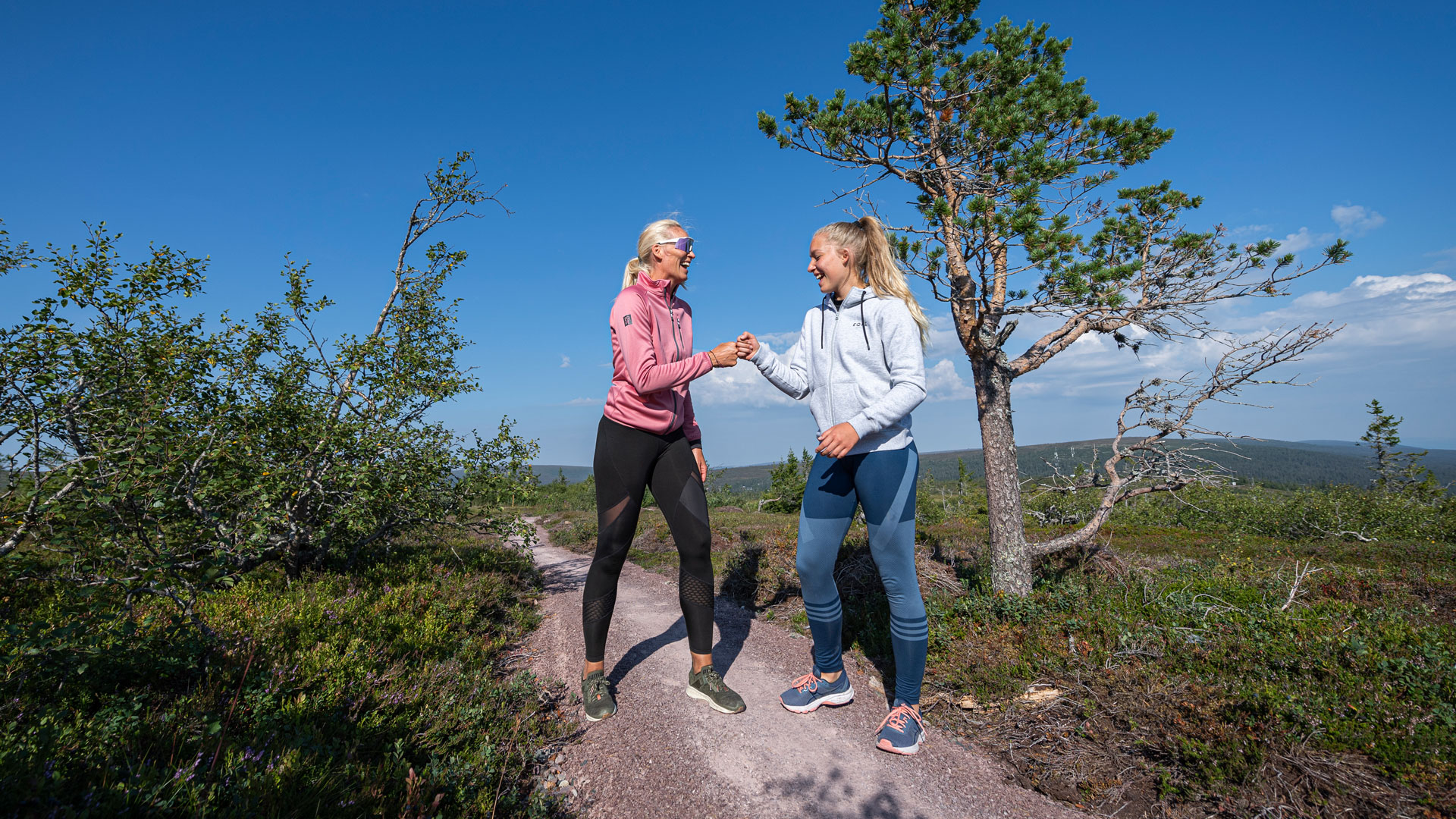 Två kvinnor som vandrar och firar på en skogsstig i fjällen under en solig dag